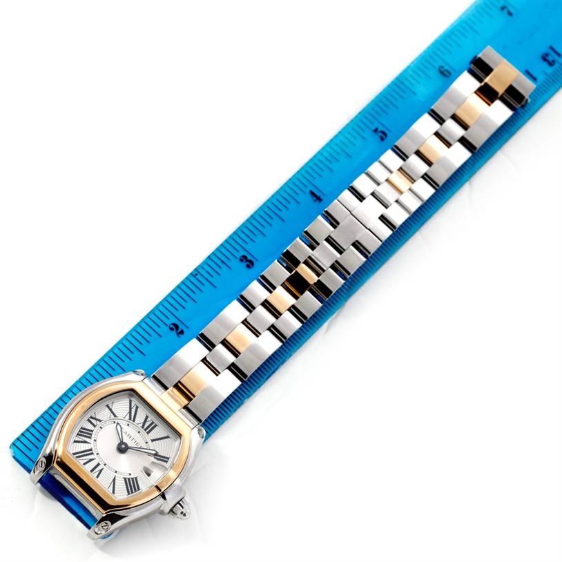 The image shows a Cartier Roadster W62026Y4 Women's Steel and Gold (two tone) Silver Dial W62026Y4 Women's Steel and Gold (two tone) Silver Dial watch with its face and metal bracelet aligned next to a blue ruler for measurement.