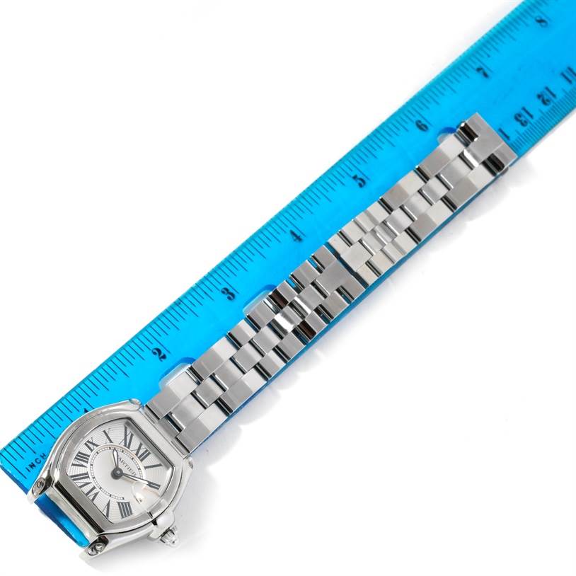 The image shows a Cartier Roadster W62016V3 Women's Stainless Steel Silver Dial W62016V3 Women's Stainless Steel Silver Dial watch with a silver bracelet and the face partially measured against a blue ruler.