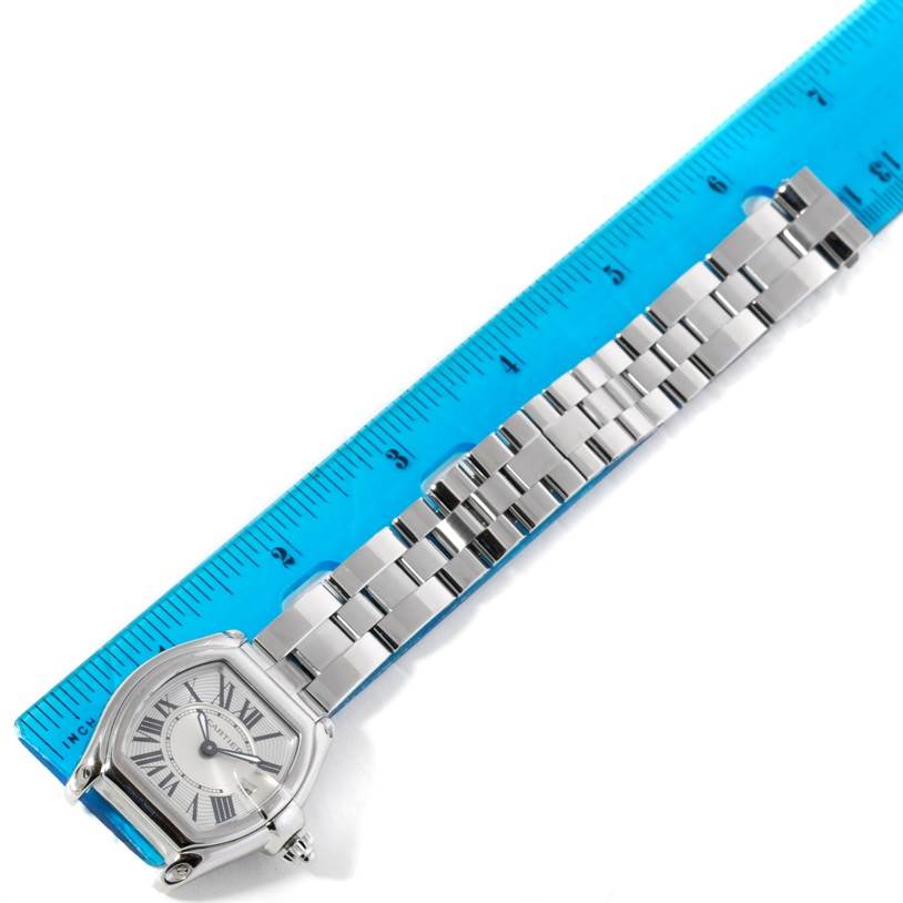 This is a top-down view of a Cartier Roadster W62016V3 Women's Stainless Steel Silver Dial W62016V3 Women's Stainless Steel Silver Dial watch showing the face and metal bracelet next to a blue ruler.