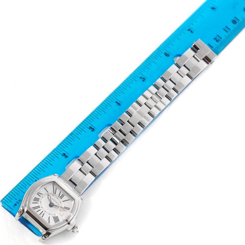 The image shows an overhead view of a Cartier Roadster W62016V3 Women's Stainless Steel Silver Dial W62016V3 Women's Stainless Steel Silver Dial watch with its bracelet laid alongside a blue ruler.