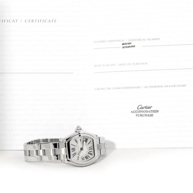 The image shows a Cartier Roadster W62016V3 Women's Stainless Steel Silver Dial W62016V3 Women's Stainless Steel Silver Dial watch laid flat with its certificate of authenticity displayed behind it.