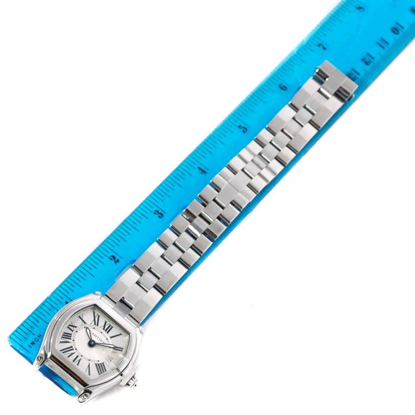 The Cartier Roadster W62016V3 Women's Stainless Steel Silver Dial W62016V3 Women's Stainless Steel Silver Dial watch is shown from a top-down angle, showcasing its face, bracelet, and clasp alongside a blue ruler.