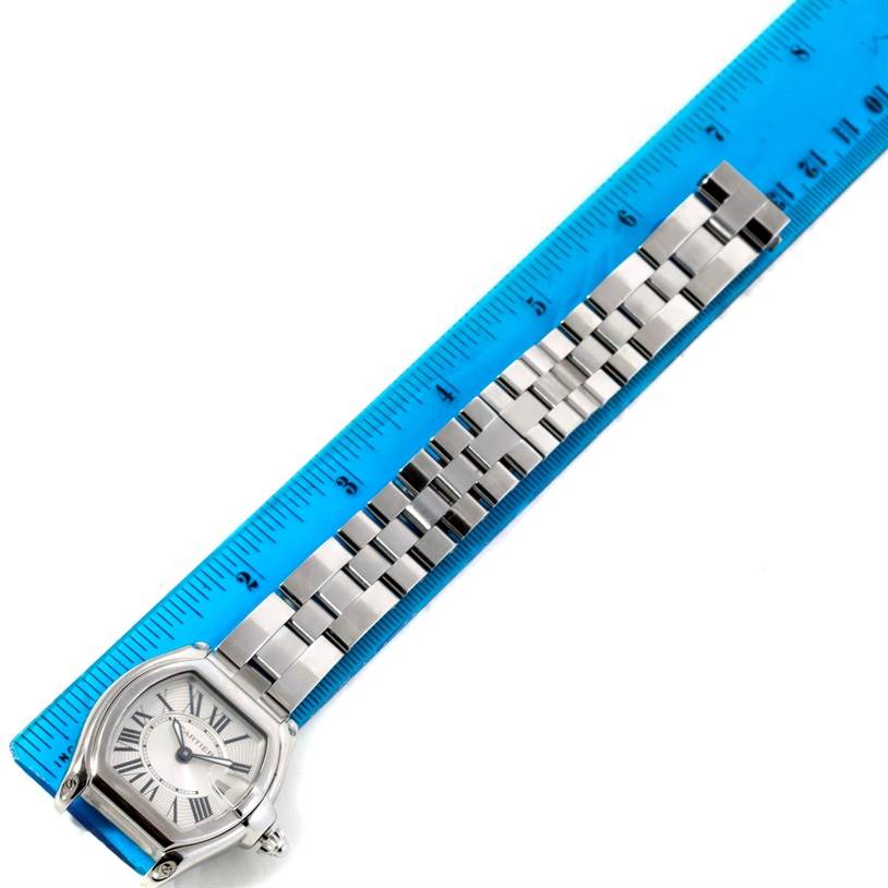 The image shows a top view of a Cartier Roadster W62016V3 Women
s Stainless Steel Silver Dial W62016V3 Women
s Stainless Steel Silver Dial watch alongside a blue ruler, highlighting the watch
s face and metal bracelet.