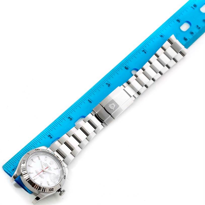 The Rolex Turn-o-Graph 116264 Men
s Stainless Steel White Dial 116264 Men
s Stainless Steel White Dial watch is shown from a top-down angle, highlighting the dial, bezel, and bracelet beside a blue ruler.