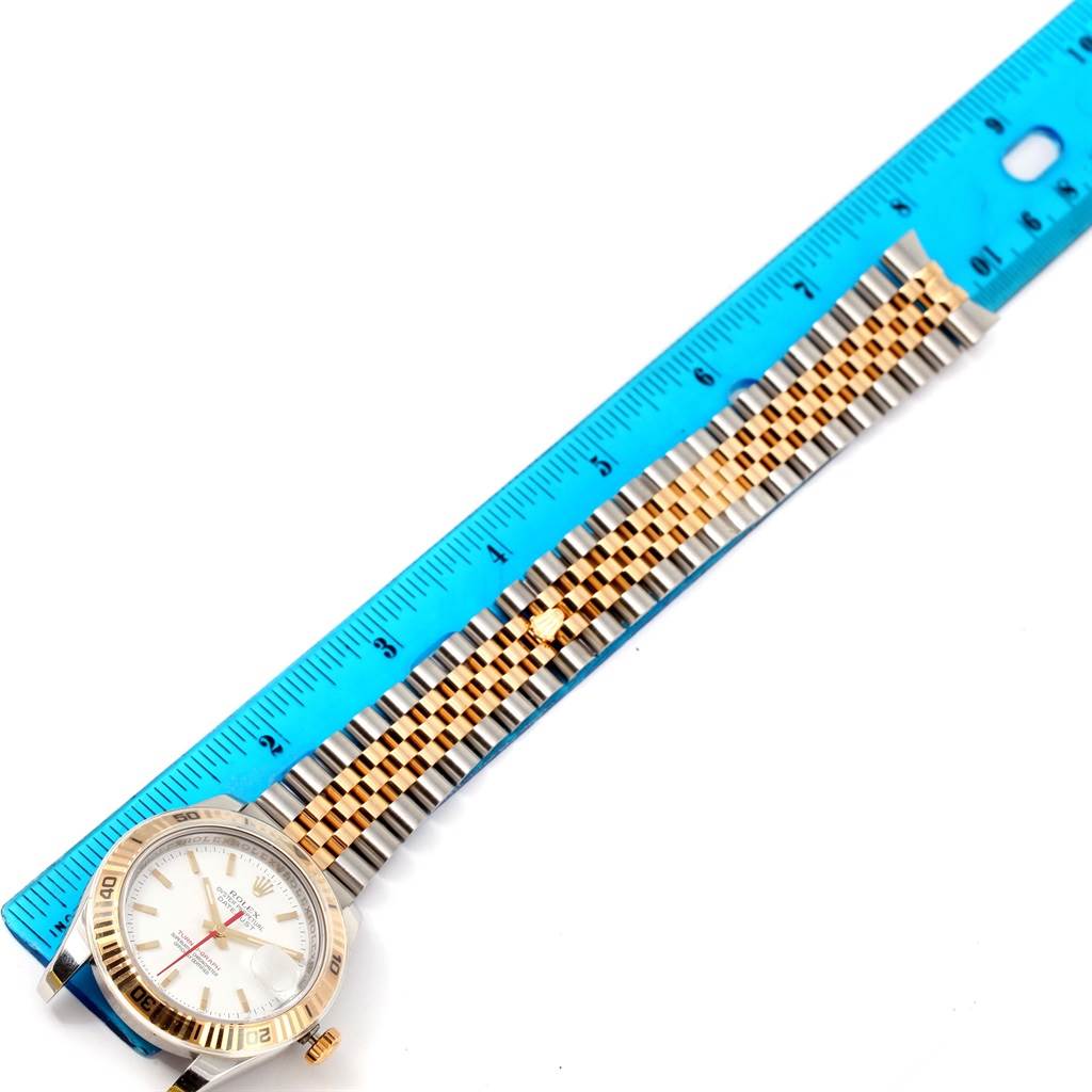 The image shows a top-down view of a Rolex Turn-o-Graph 116263 Men's Stainless Steel White Dial 116263 Men's Stainless Steel White Dial watch next to a ruler, highlighting its face and linked bracelet.