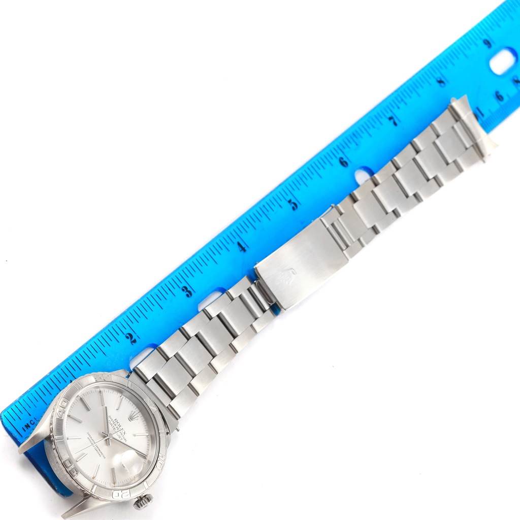 The image shows a Rolex Turn-o-Graph 16264 Men's Stainless Steel Silver Dial 16264 Men's Stainless Steel Silver Dial watch laid flat with its stainless steel band and clasp alongside a blue ruler for scale.