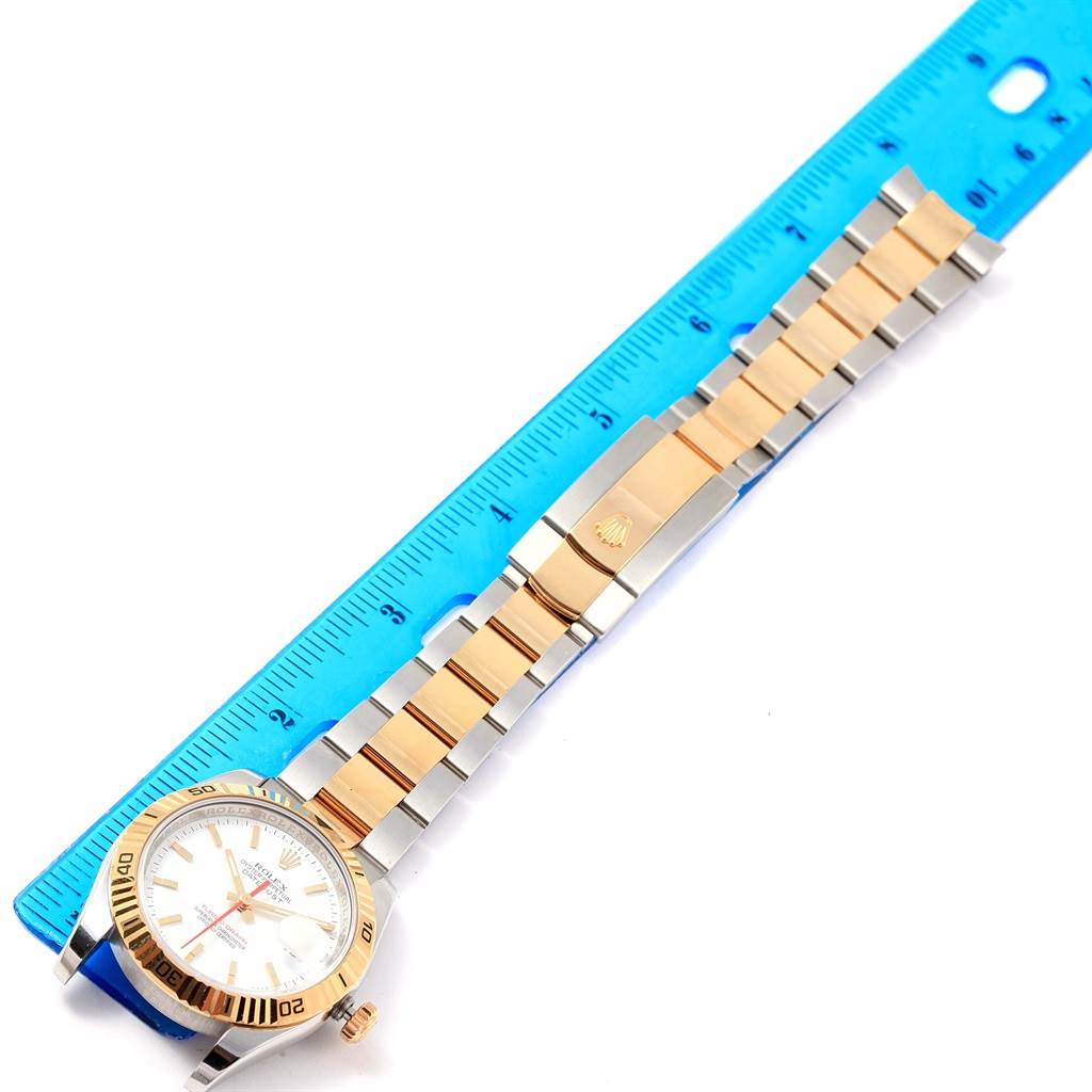 The Rolex Turn-o-Graph 116263 Men
s Stainless Steel White Dial 116263 Men
s Stainless Steel White Dial watch is shown at an angled top view, along with its band and a blue ruler for scale.