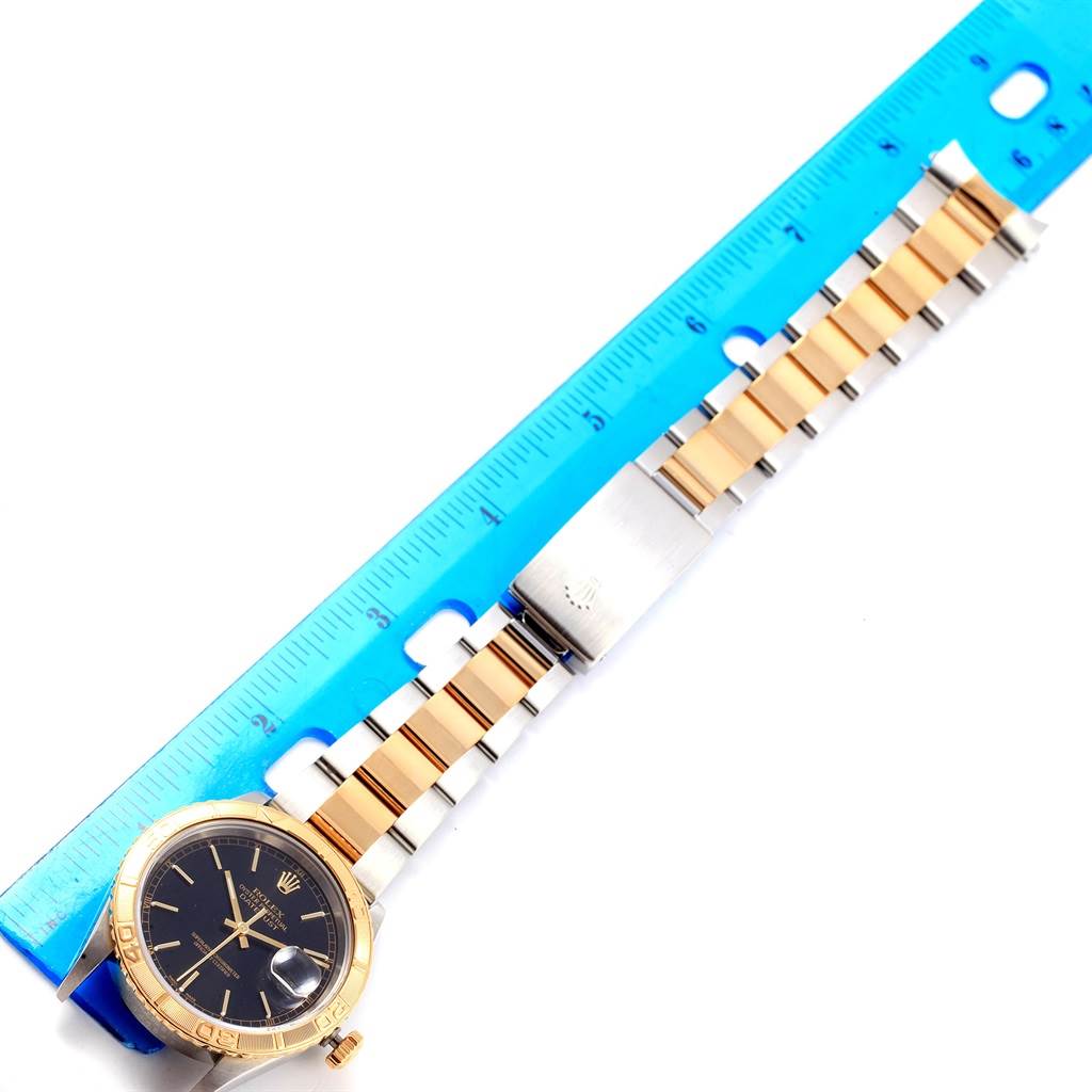 The Rolex Turn-o-Graph 16263 Men's Steel and Gold (two tone) Black Dial 16263 Men's Steel and Gold (two tone) Black Dial watch is shown from above, displaying the dial, bezel, bracelet, and clasp next to a blue ruler.