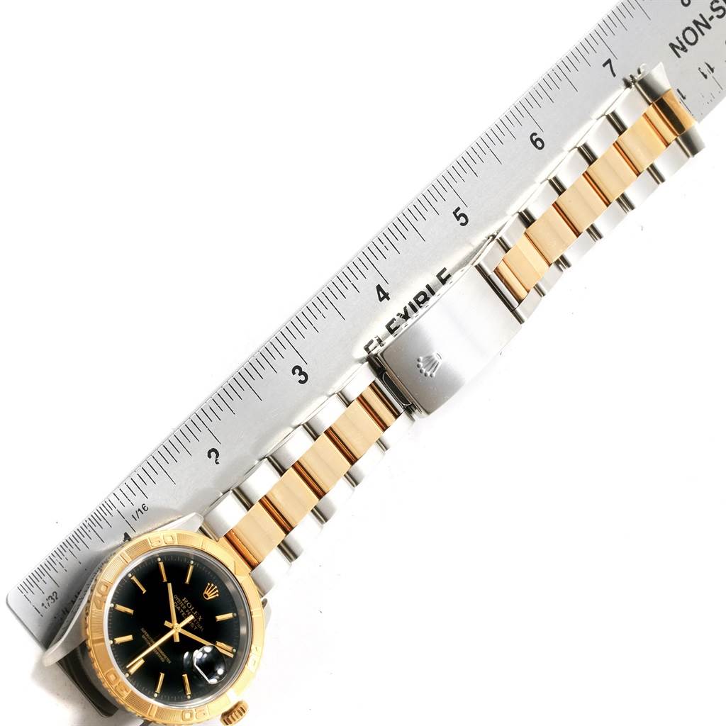 This image of a Rolex Turn-o-Graph 16263 Men's Steel and Gold (two tone) Black Dial 16263 Men's Steel and Gold (two tone) Black Dial watch shows the face, bezel, and part of the metal bracelet, lined up against a ruler.
