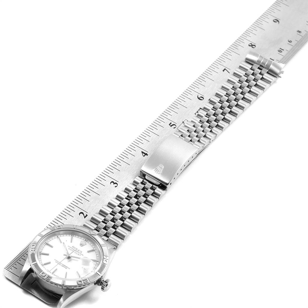 The Rolex Turn-o-Graph 16264 Men
s Stainless Steel White Dial 16264 Men
s Stainless Steel White Dial watch is shown from a top-down angle, featuring the face, bezel, bracelet, and clasp laid next to a ruler.