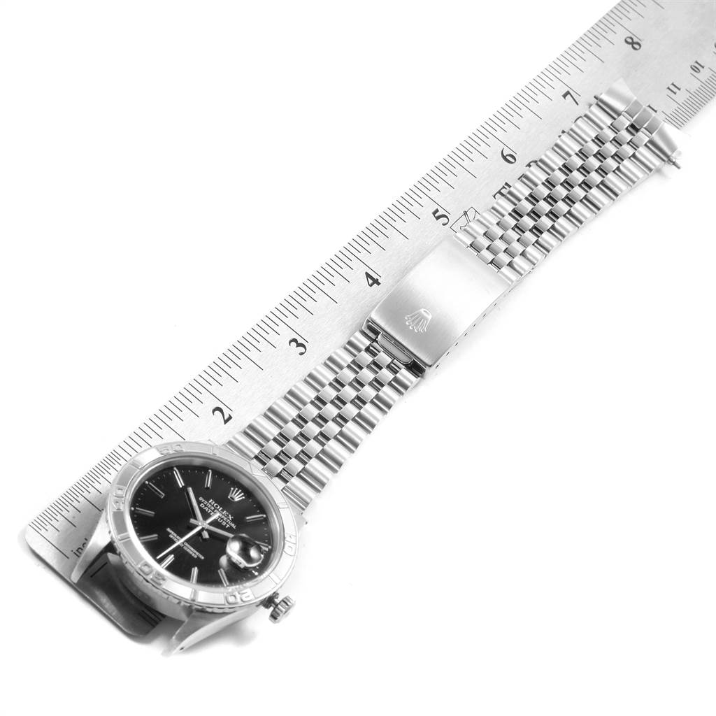 The image shows a Rolex Turn-o-Graph 16264 Men
s Stainless Steel Black Dial 16264 Men
s Stainless Steel Black Dial watch laying flat next to a ruler, highlighting the face, bezel, and part of the metal bracelet.