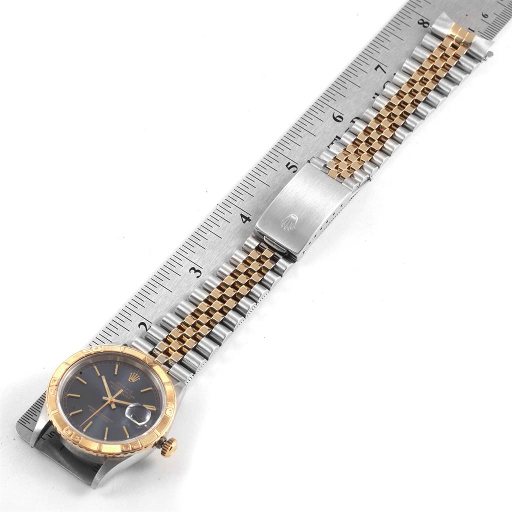 The image shows a Turn-o-Graph Rolex watch laid flat on a ruler, displaying the watch face, crown, and bracelet with clasp.