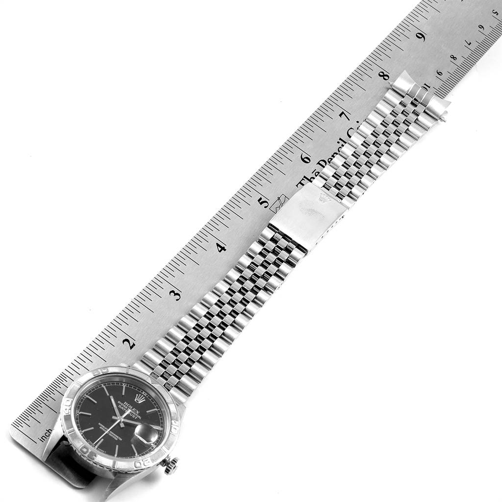 The image shows a Rolex Turn-o-Graph 16264 Men
s Stainless Steel Black Dial 16264 Men
s Stainless Steel Black Dial watch lying flat with a ruler measuring its length, showcasing the watch face, bracelet, and clasp.