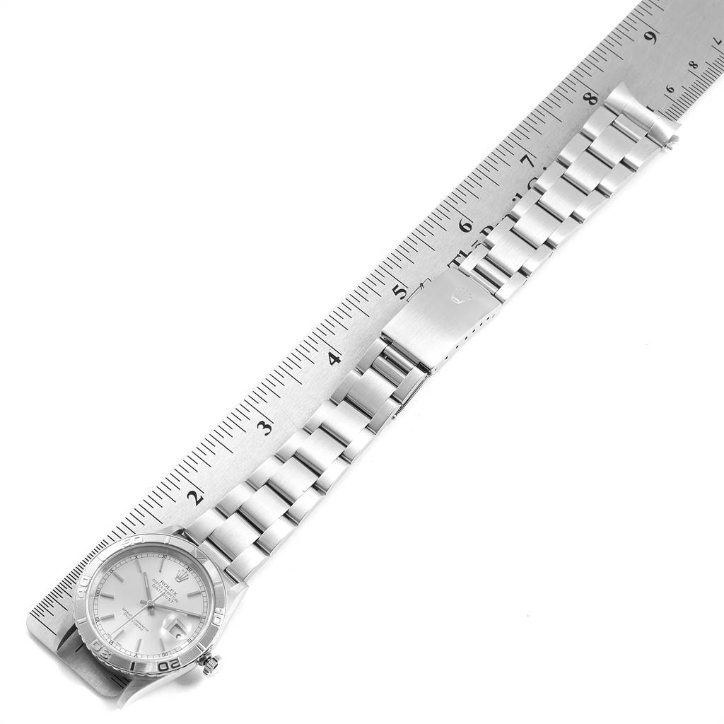 The image shows an overhead view of a Rolex Turn-o-Graph 16264 Men
s Stainless Steel Silver Dial 16264 Men
s Stainless Steel Silver Dial watch with a metal bracelet and clasp positioned next to a ruler.