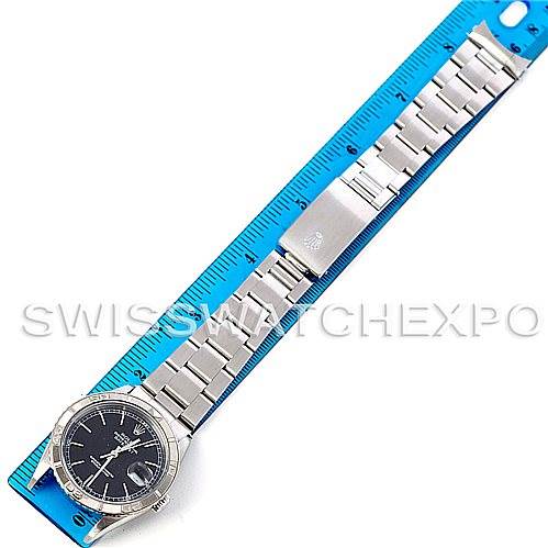 The image shows a top-down view of a Rolex Turn-o-Graph 16264 Men
s Stainless Steel Black Dial 16264 Men
s Stainless Steel Black Dial watch, displaying its face, bezel, and metal bracelet against a blue ruler.