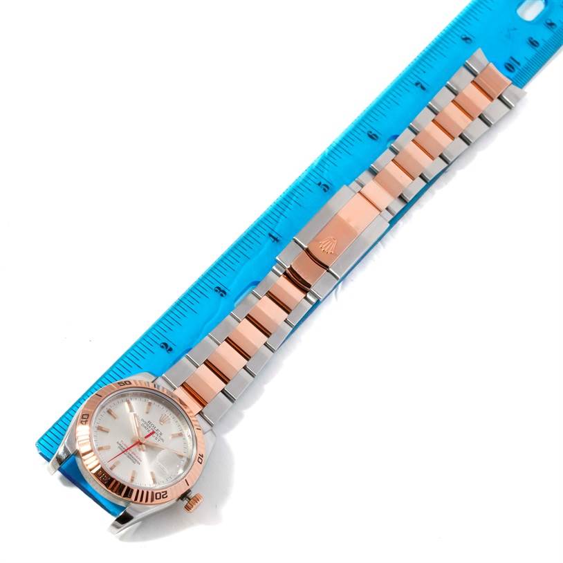 The Rolex Turn-o-Graph 116261 Men
s Stainless Steel Silver Dial 116261 Men
s Stainless Steel Silver Dial watch is shown from a top-down view, displaying the face, bezel, and entirety of the bracelet against a ruler.