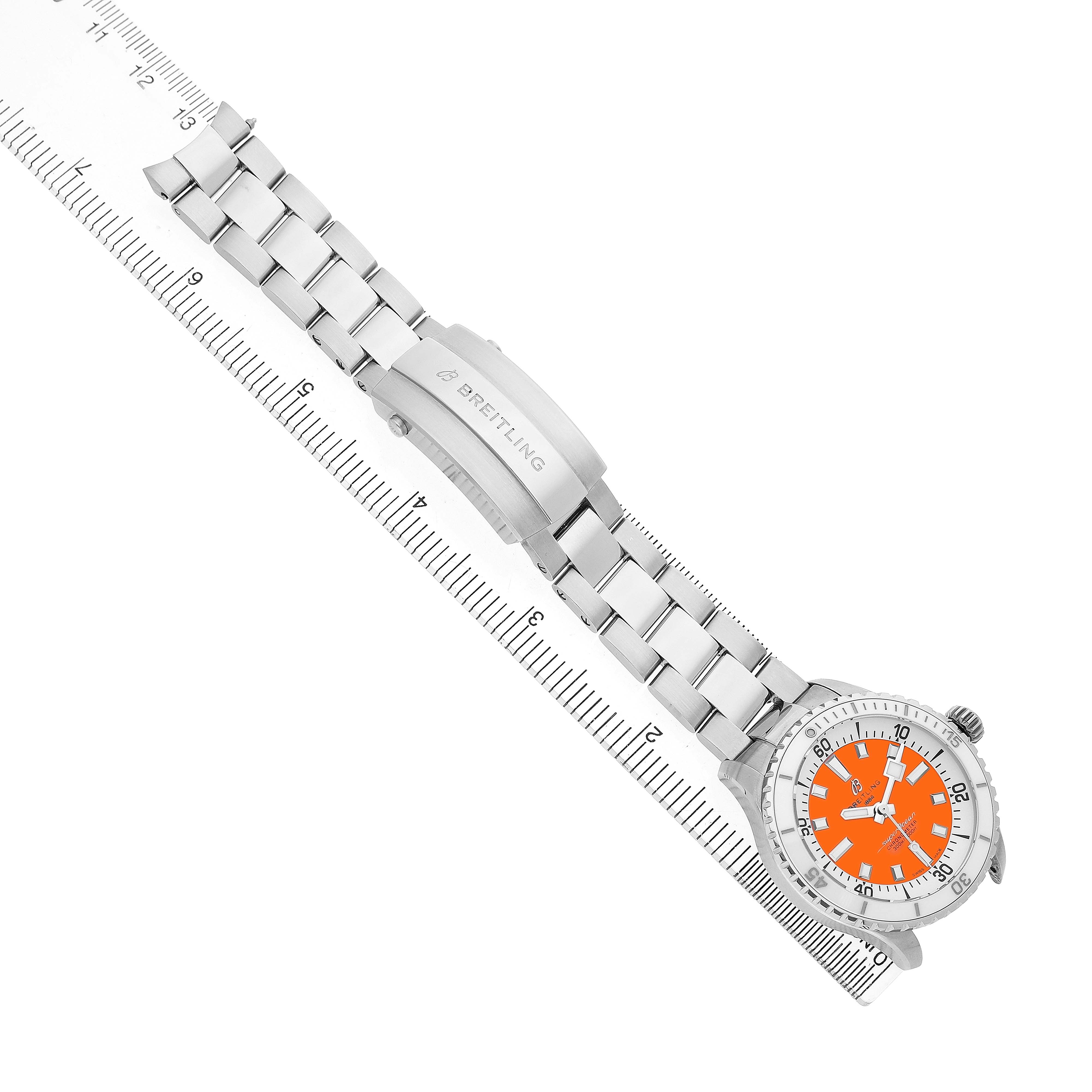 The Breitling A17377 Women's Stainless Steel Orange Dial Superocean 36 watch is shown from above, highlighting its orange dial, steel bracelet, and clasp aligned with a ruler.