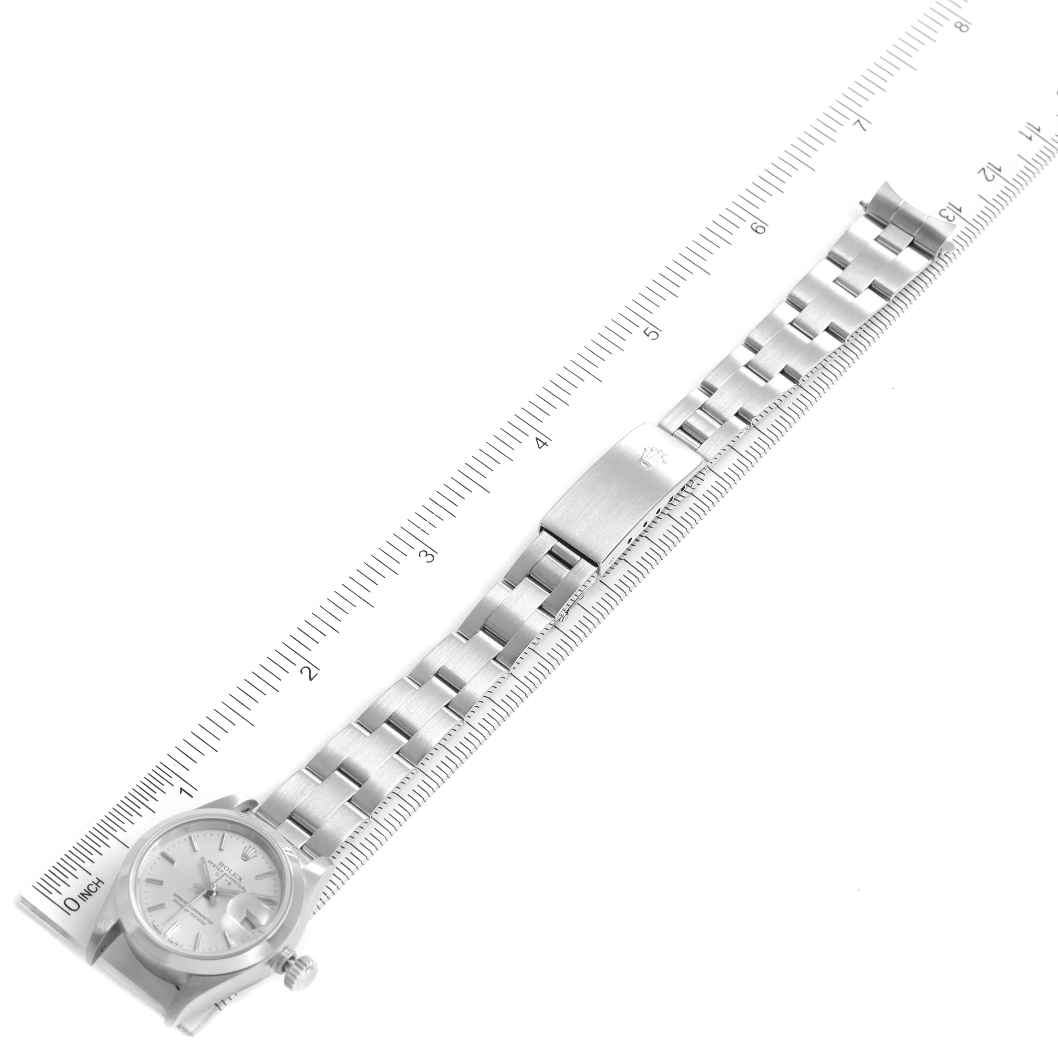 The image shows a top view of a Rolex Date 69160 Women
s Stainless Steel Silver Dial 69160 Women
s Stainless Steel Silver Dial model watch with its watch face, bracelet, and clasp against a measuring ruler.