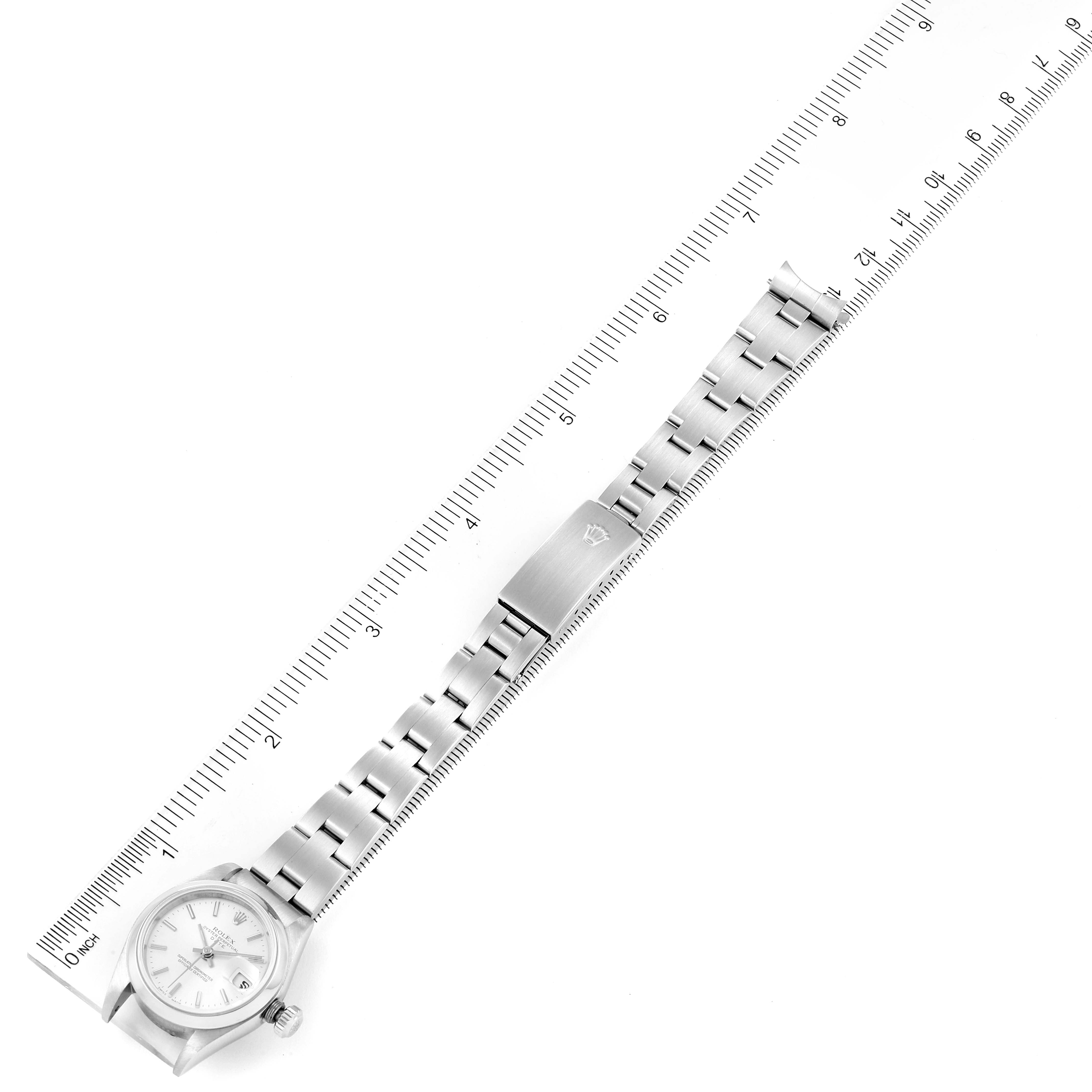 This image shows a top view of a Rolex Date 79160 Women's Stainless Steel Silver Dial 79160 Women's Stainless Steel Silver Dial model watch with its band extended next to a ruler for scale.