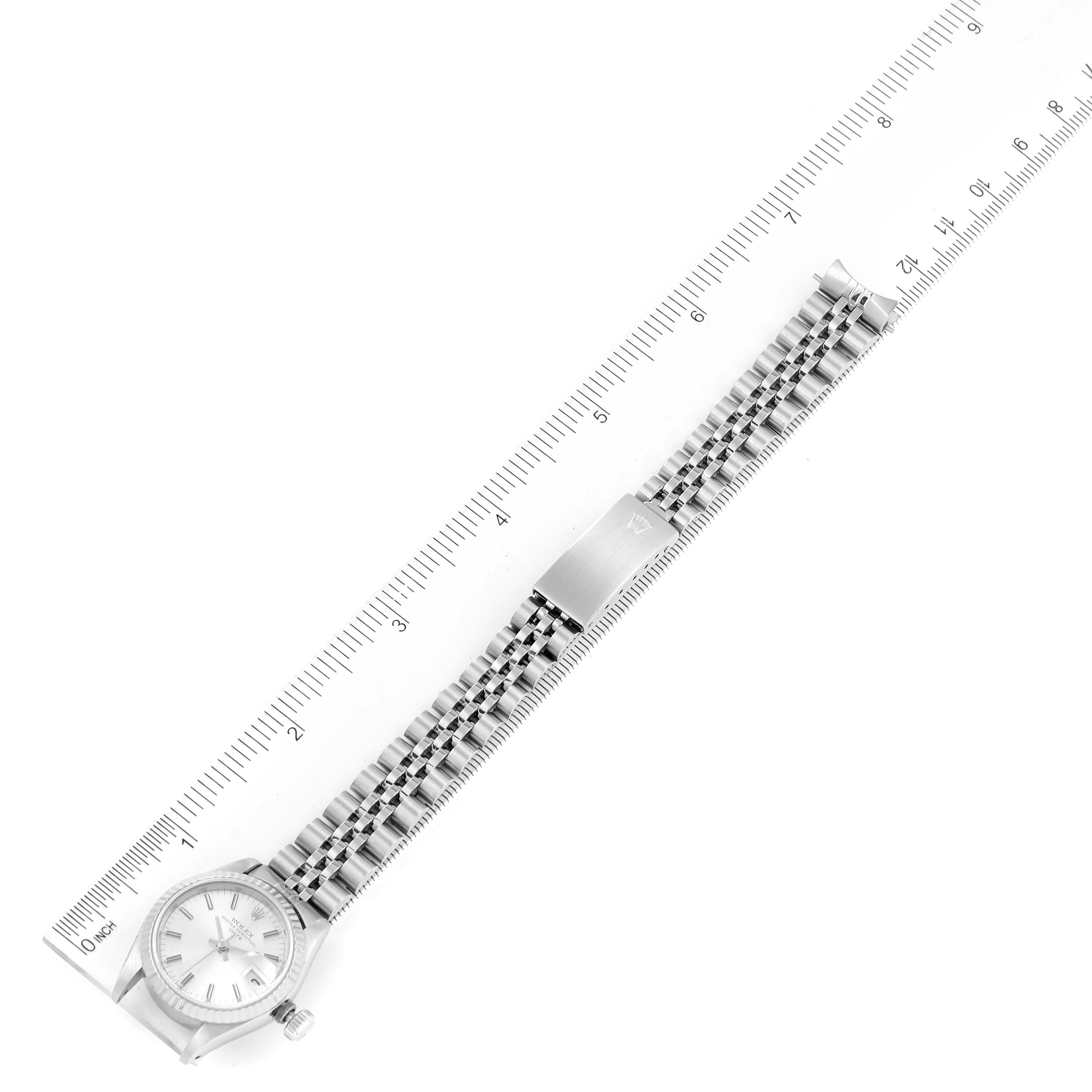 The Rolex Date 69174 Women's Stainless Steel Silver Dial 69174 Women's Stainless Steel Silver Dial model watch is shown from a top-down angle beside a ruler, displaying its face, bracelet, and clasp.