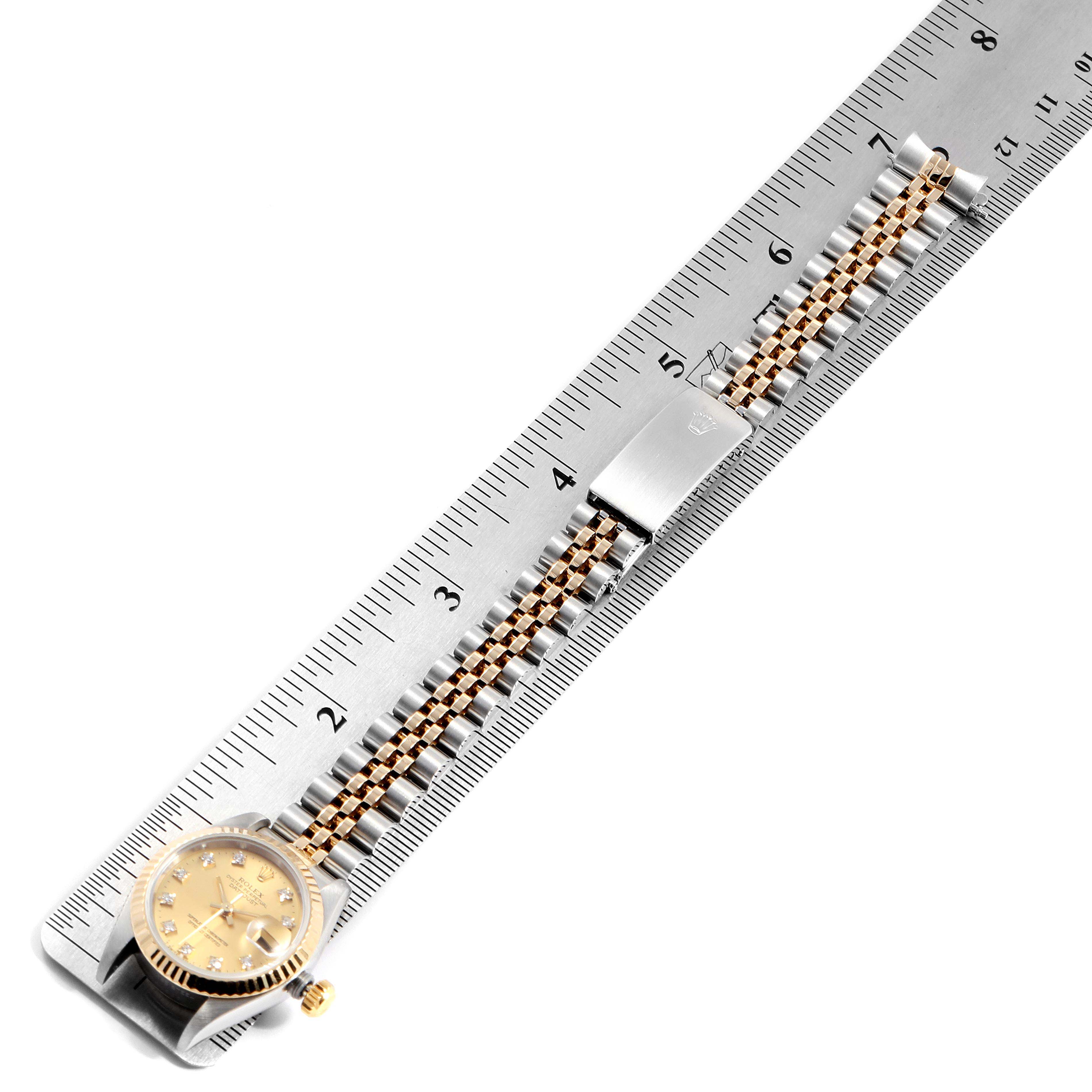 This image shows a Rolex Datejust 69173 Women
s Steel and Gold (two tone) Champagne Dial 69173 Women
s Steel and Gold (two tone) Champagne Dial watch laid flat against a ruler, displaying the watch face, crown, and bracelet.
