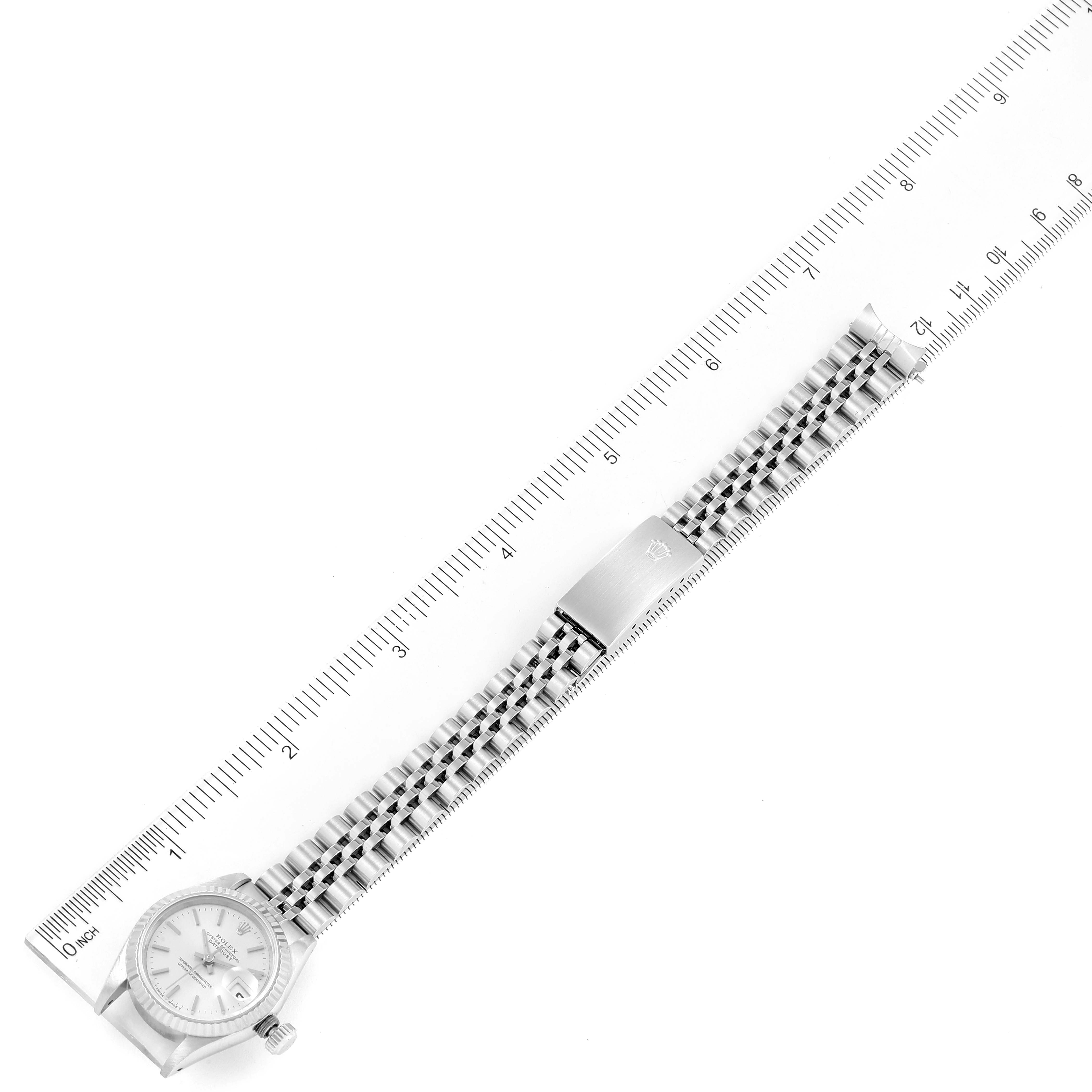 The Rolex Datejust 69174 Women
s Stainless Steel Silver Dial 69174 Women
s Stainless Steel Silver Dial watch is shown from a top-down angle, fully extended, alongside a ruler for scale.