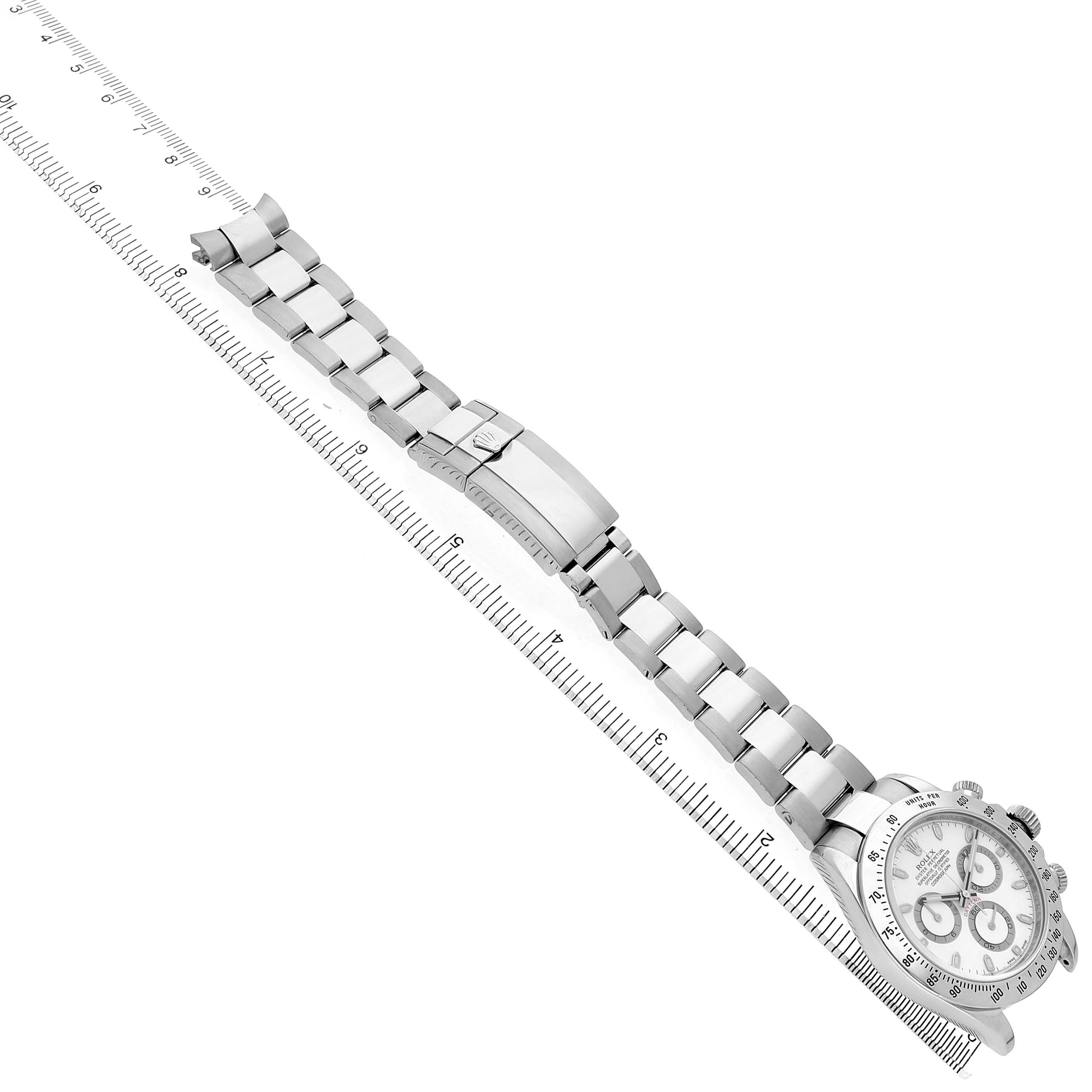 The image shows a Rolex Daytona 116520 Men's Stainless Steel White Dial watch laid flat with its metal bracelet extended, positioned diagonally on a ruler.
