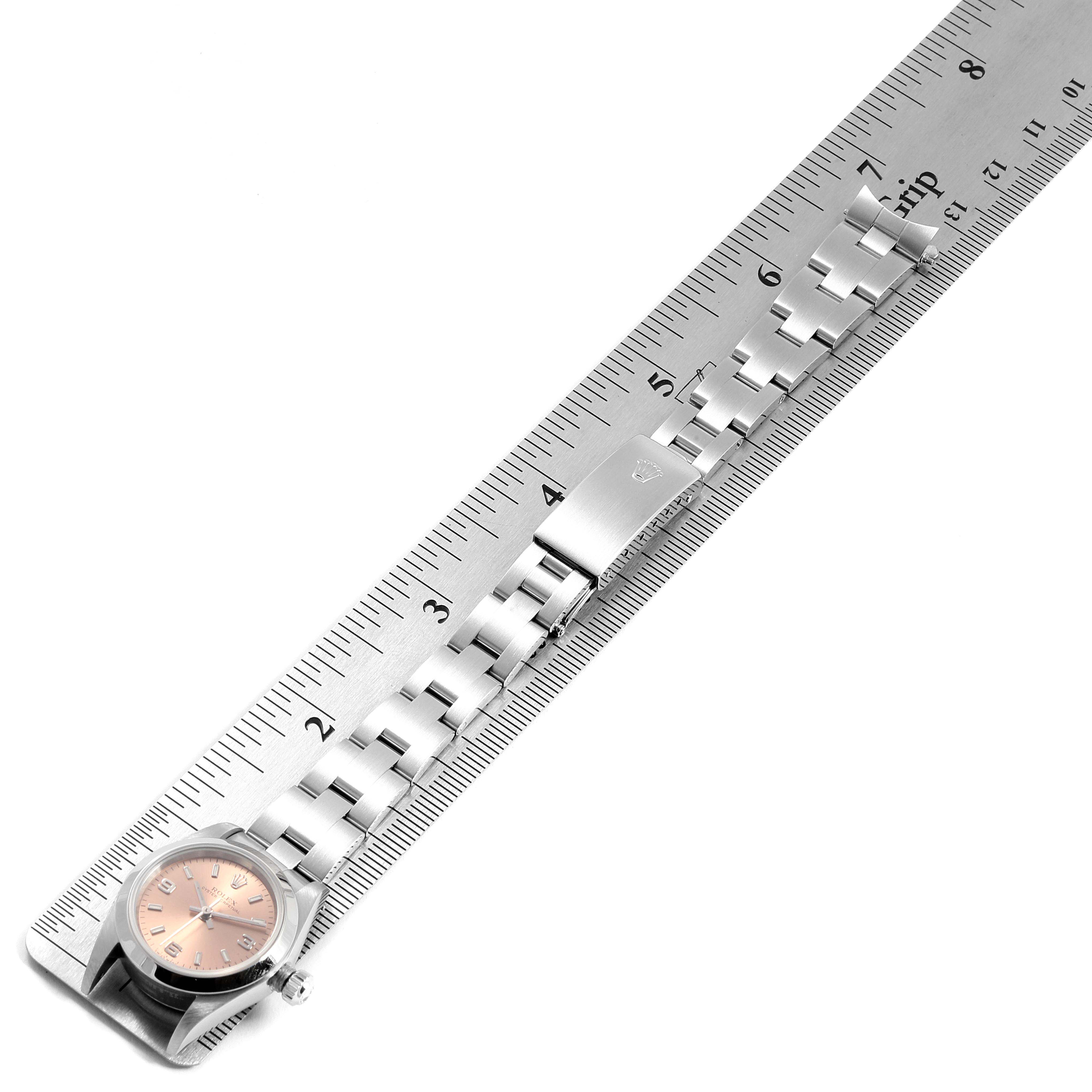 The image shows a Rolex Oyster Perpetual 76080  Women's Stainless Steel Pink Dial 76080  Women's Stainless Steel Pink Dial watch lying flat on a ruler, highlighting the clasp, bracelet, and face.