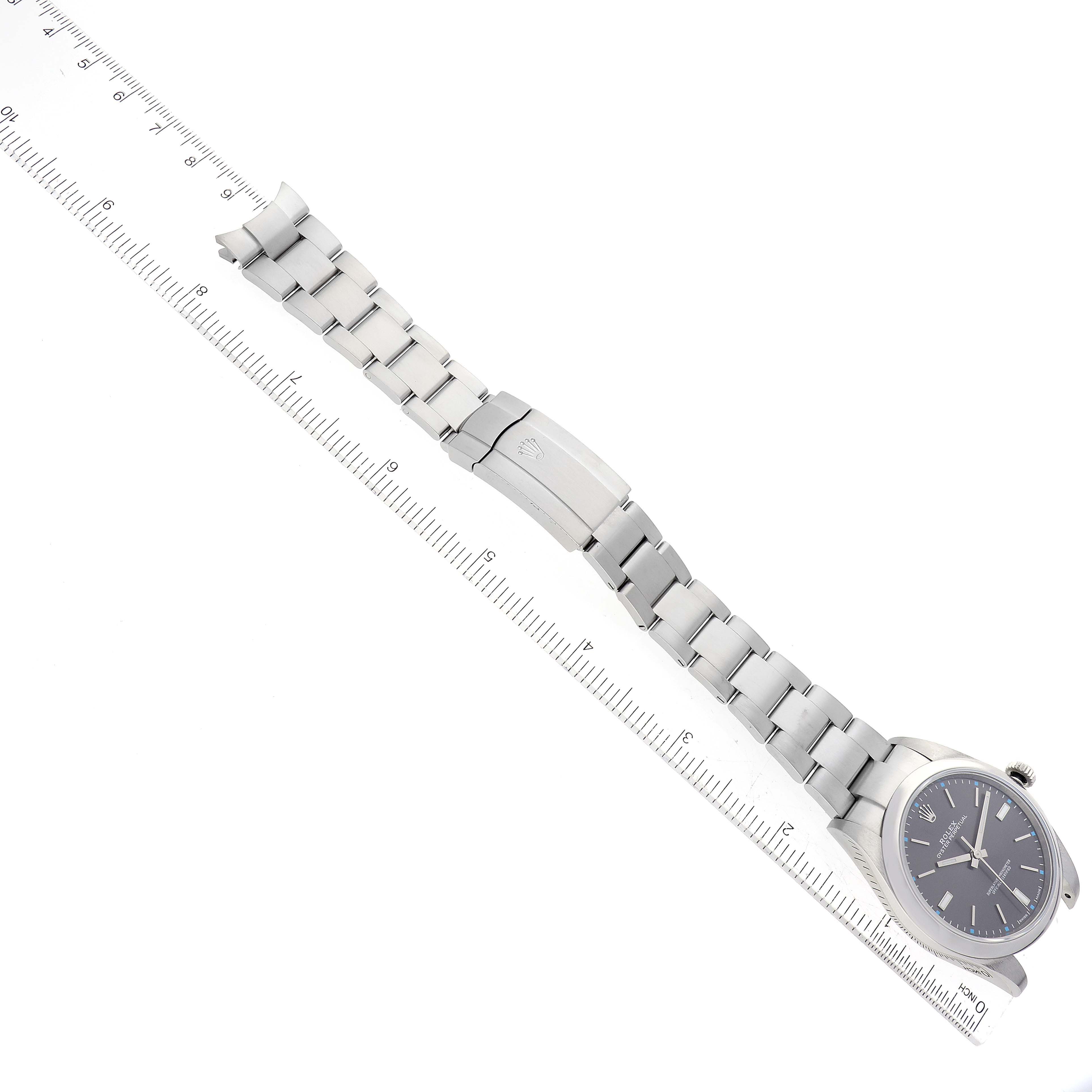 The image shows a Rolex Oyster Perpetual 114300 Men's Stainless Steel Grey Dial 114300 Men's Stainless Steel Grey Dial watch laid flat with the bracelet extended and aligned next to a ruler.