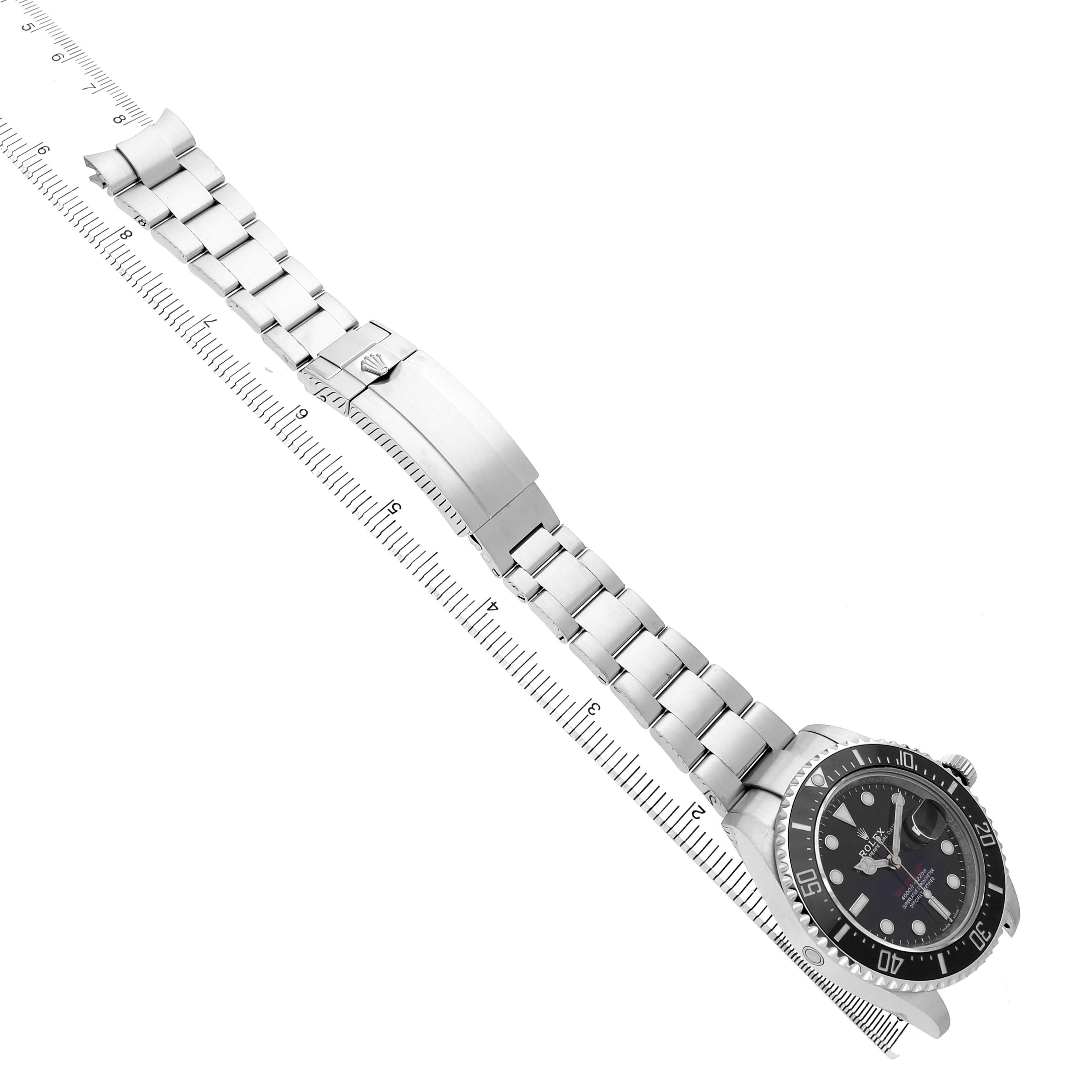 The Rolex Sea-Dweller 126600 Men's Stainless Steel Black Dial watch is shown from a top-down angle, displaying the full bracelet and clasp alongside a ruler for scale.