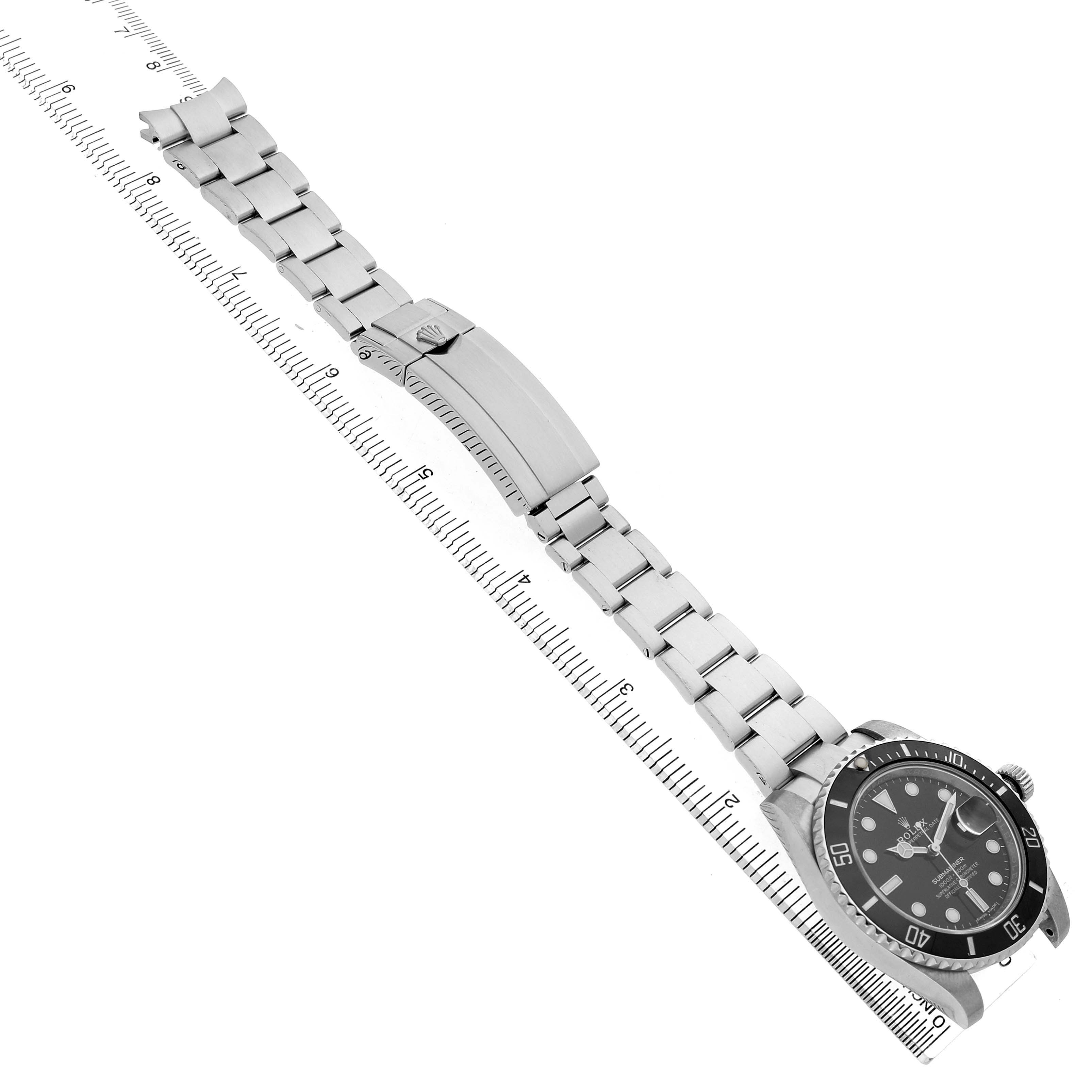 The Rolex Submariner 116610 Men's Stainless Steel Black Dial watch is shown at an angled side view, highlighting its bracelet, clasp, and face with a ruler for scale.
