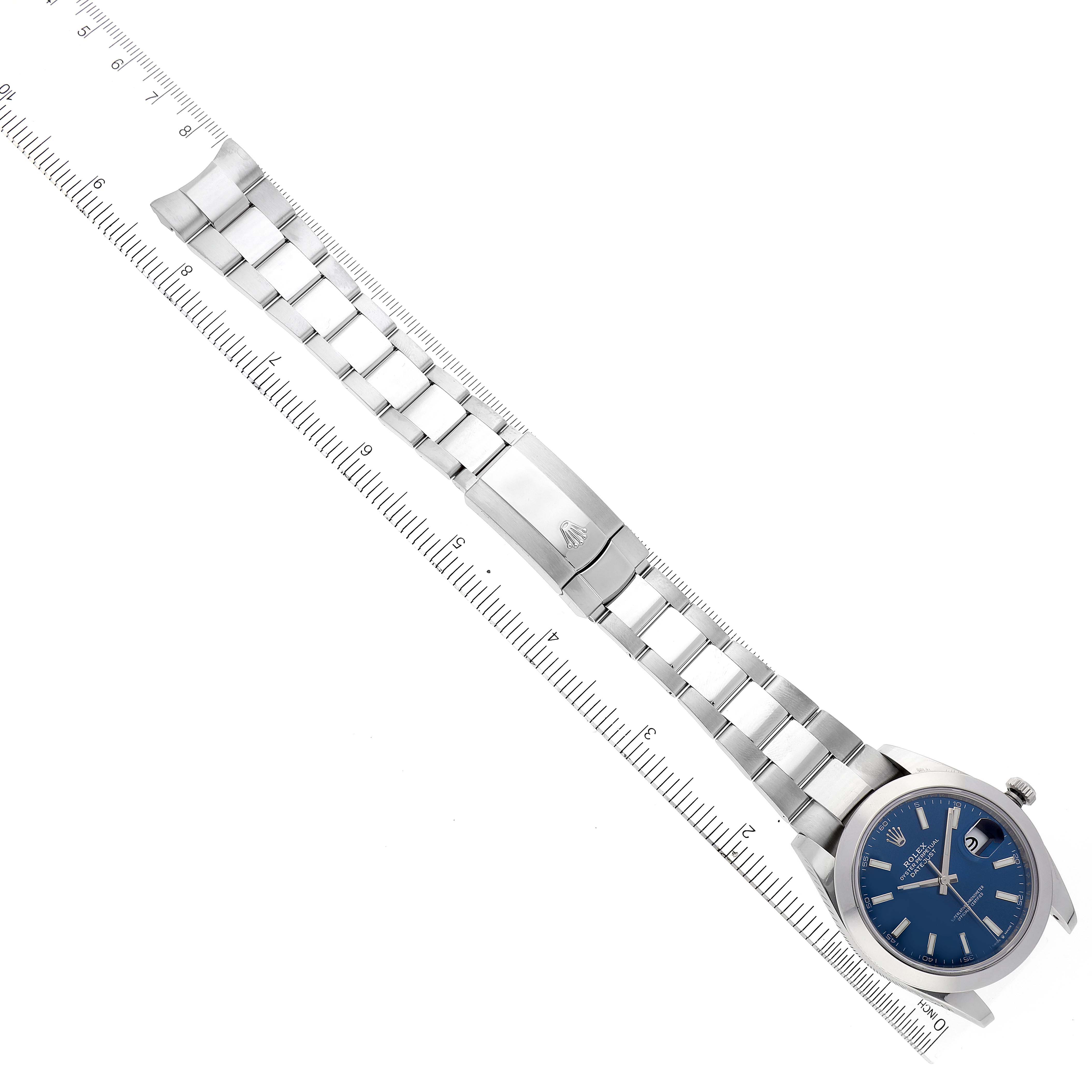The image shows a top-down view of a Rolex Datejust 41 126300 Men's Stainless Steel Blue Dial 126300 Men's Stainless Steel Blue Dial watch with a blue dial and metal bracelet laid alongside a ruler.