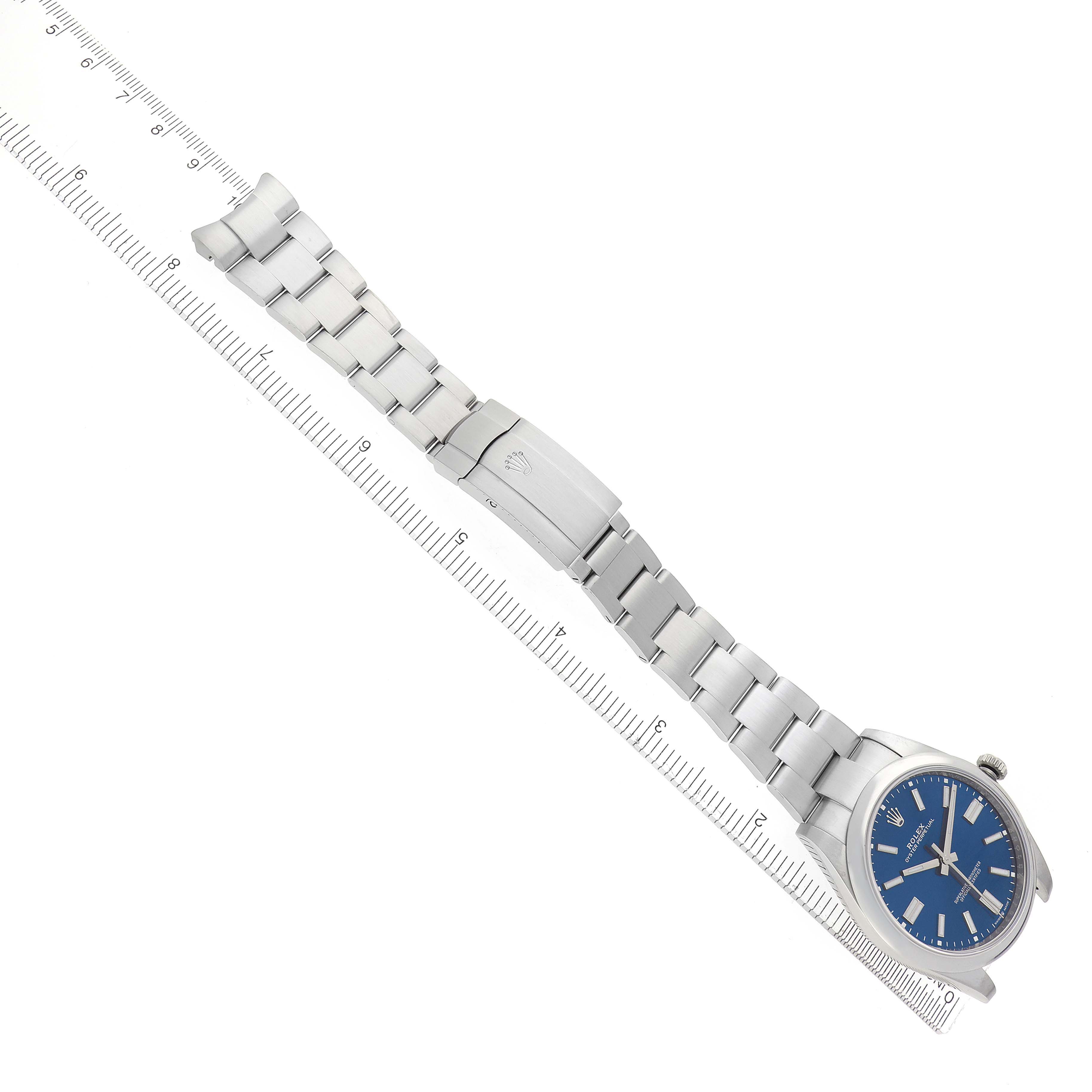 The Rolex Oyster Perpetual 124300 Men's Stainless Steel Blue Dial 124300 Men's Stainless Steel Blue Dial watch is shown from a top-down angle, displaying the full bracelet and blue dial alongside a ruler.