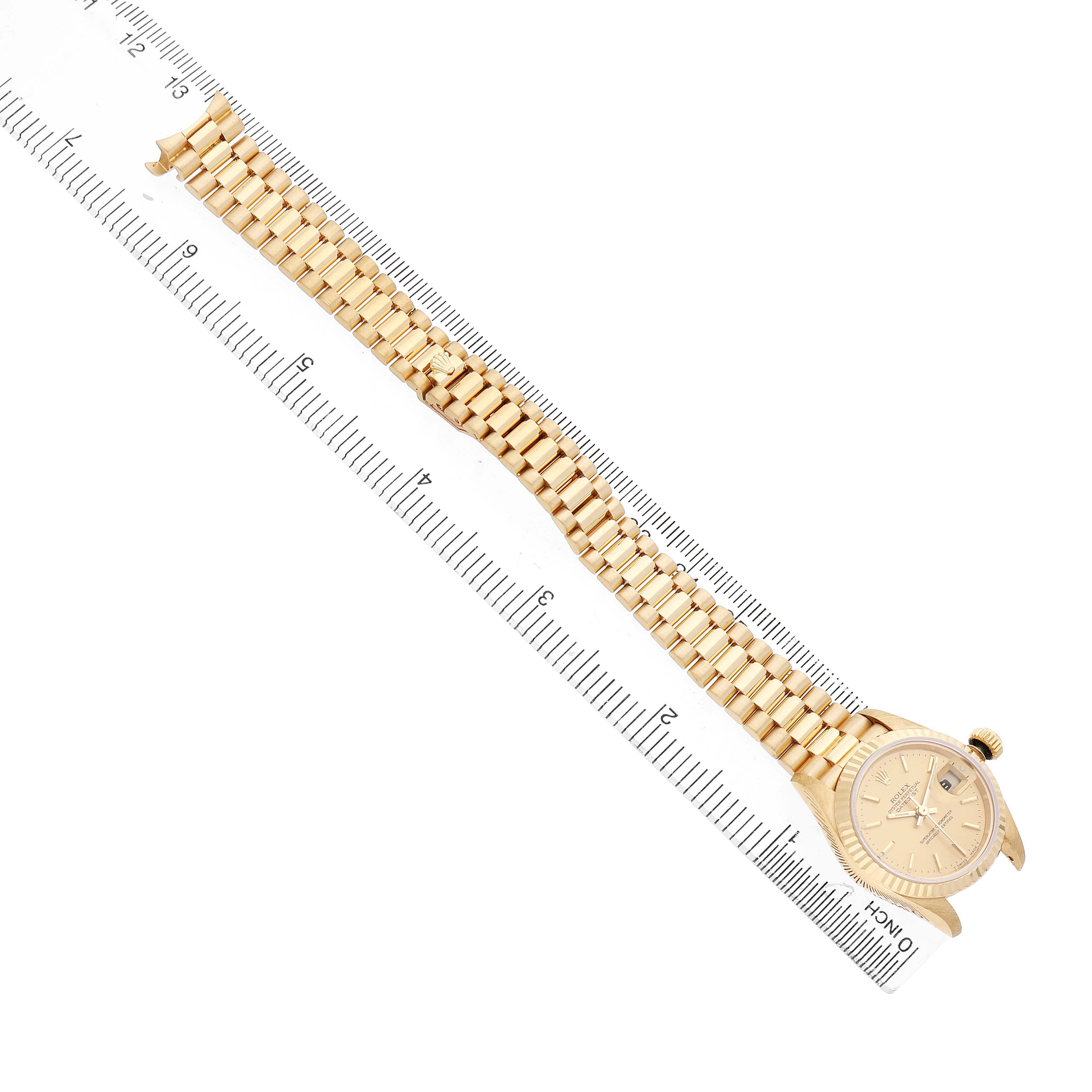 The Rolex President 69178 Women's Yellow Gold Champagne Dial watch is shown from an overhead angle, displaying the face, bezel, and full bracelet alongside a ruler.