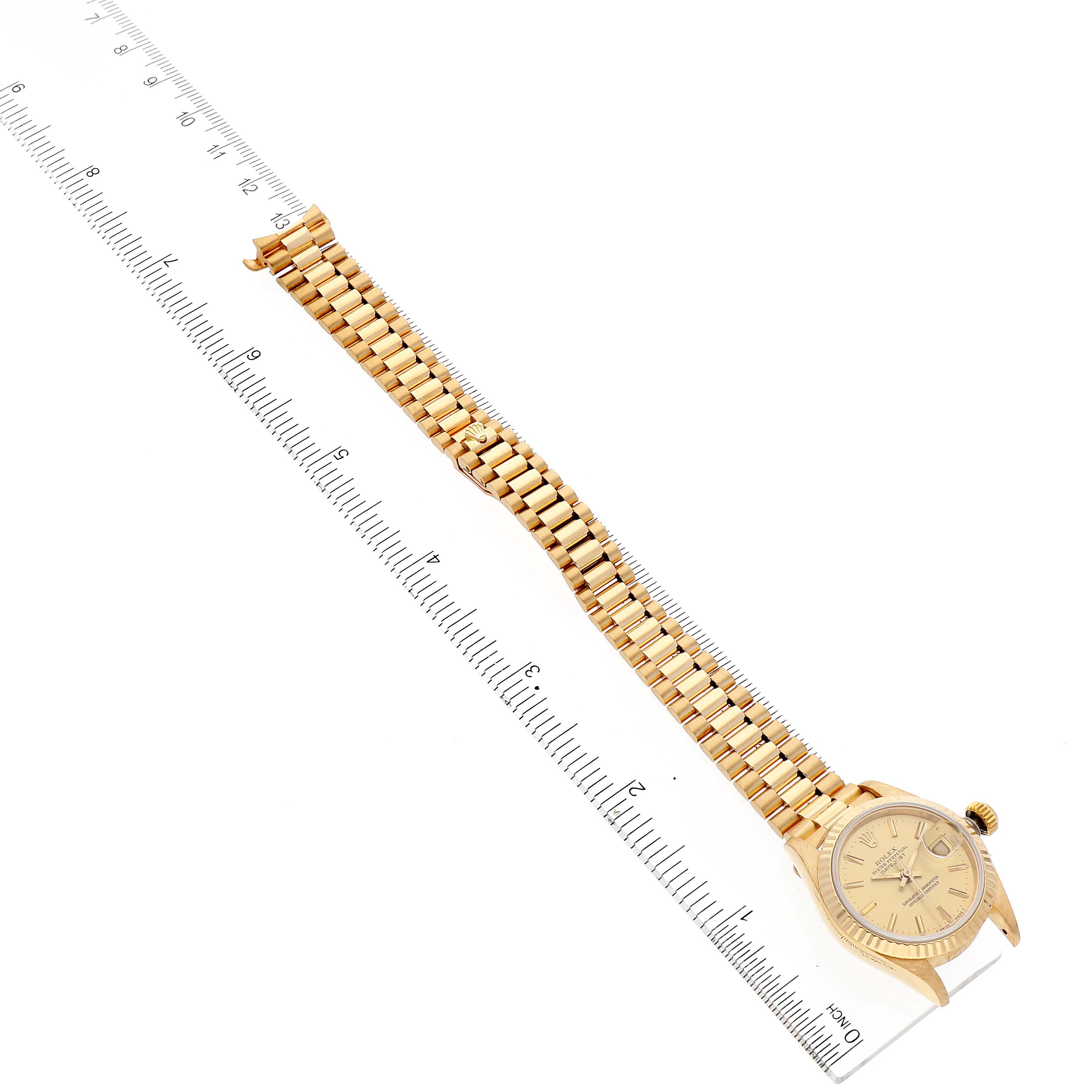 The image shows a Rolex President 69178 Women
s Yellow Gold Champagne Dial 69178 Women
s Yellow Gold Champagne Dial model watch laid flat with its bracelet fully extended alongside a ruler for measurement.