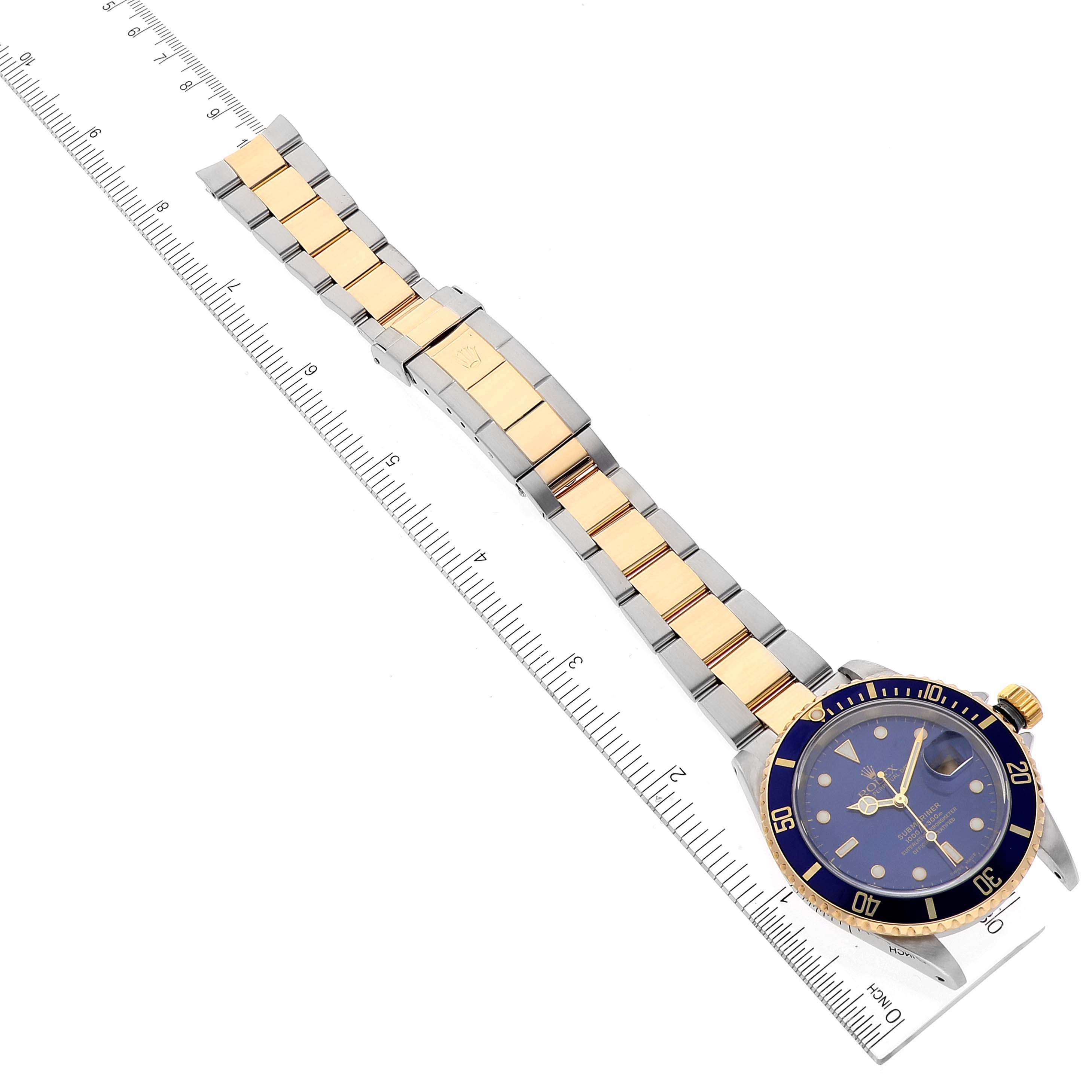 The Rolex Submariner 16613 Men
s Steel and Gold (two tone) Blue Dial 16613 Men
s Steel and Gold (two tone) Blue Dial watch is shown from an overhead angle, displaying the entire bracelet and face next to a ruler for scale.
