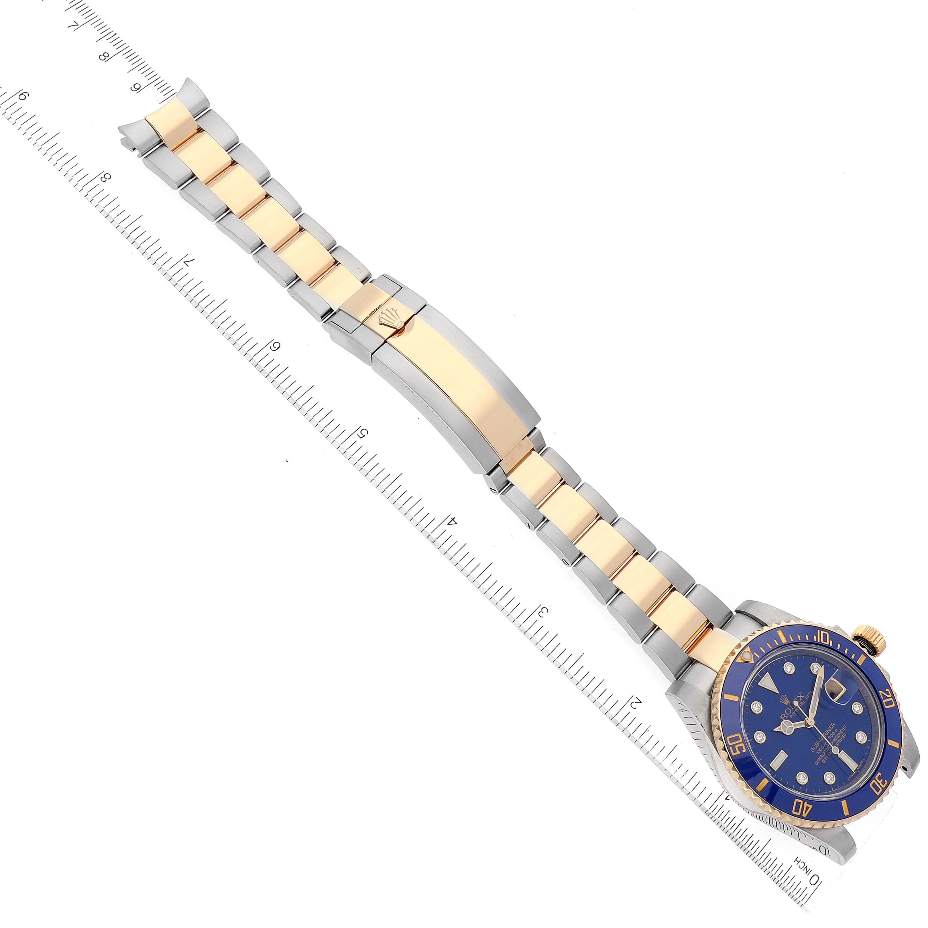 This image shows a Rolex Submariner 116613 Men's Steel and Gold (two tone) Blue Dial 116613 Men's Steel and Gold (two tone) Blue Dial watch laid flat, highlighting the gold and silver bracelet alongside a measuring scale.