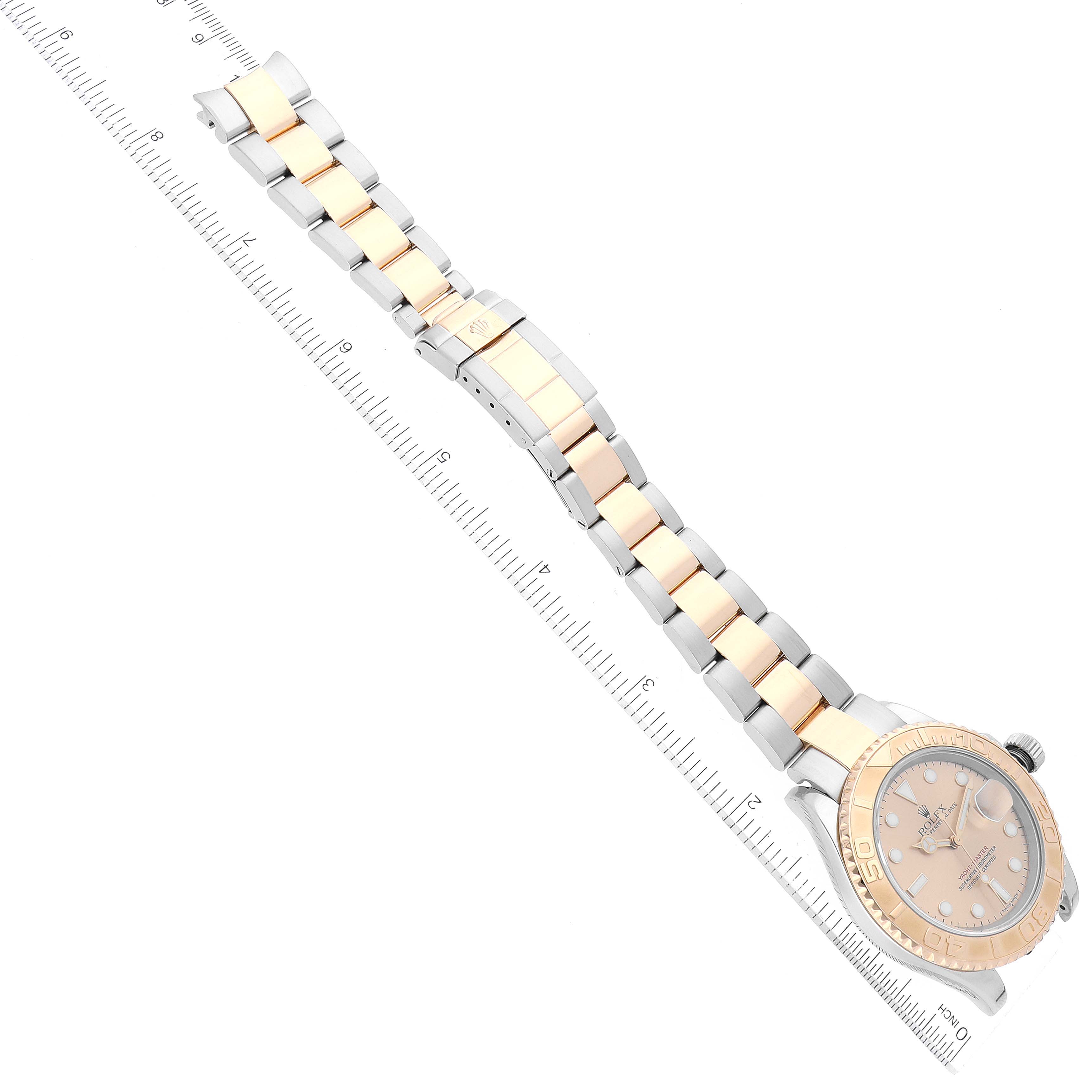 The image shows the Rolex Yacht-Master 16623 Men's Steel and Gold (two tone) Champagne Dial 16623 Men's Steel and Gold (two tone) Champagne Dial watch laid diagonally, highlighting its face and bi-tone band next to a measuring ruler.