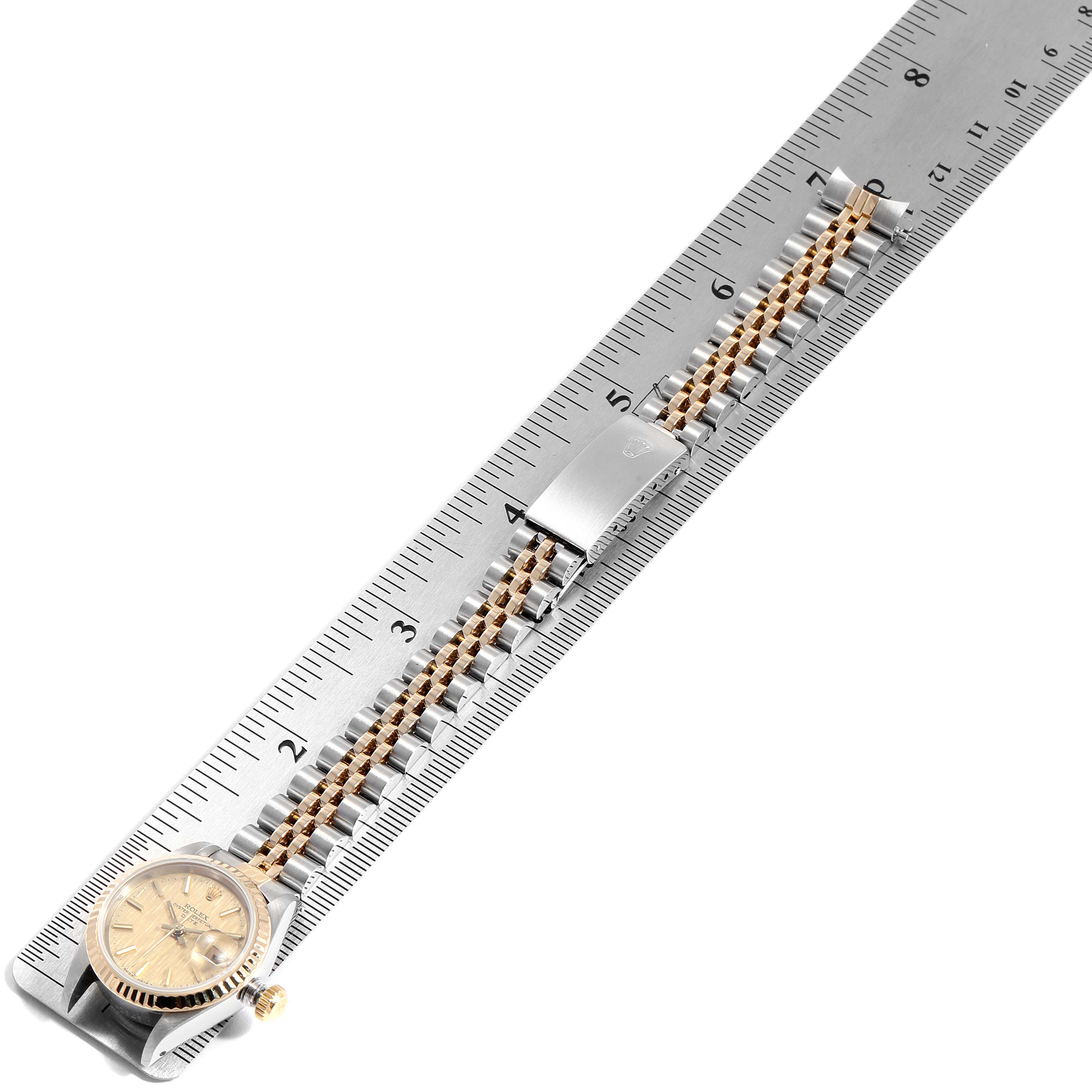 This image shows a Rolex Datejust 69173 Women
s Steel and Gold (two tone) Champagne Dial 69173 Women
s Steel and Gold (two tone) Champagne Dial watch laid flat on a ruler, displaying the watch face, crown, and two-tone bracelet.