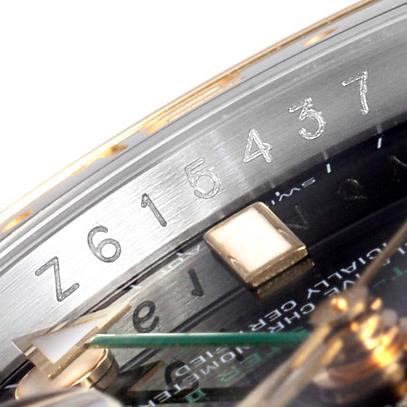 This close-up image of the Rolex GMT-Master 116713 Men's Steel and Gold (two tone) Black Dial 116713 Men's Steel and Gold (two tone) Black Dial shows part of the bezel, the dial, and the serial number engraved on the case.