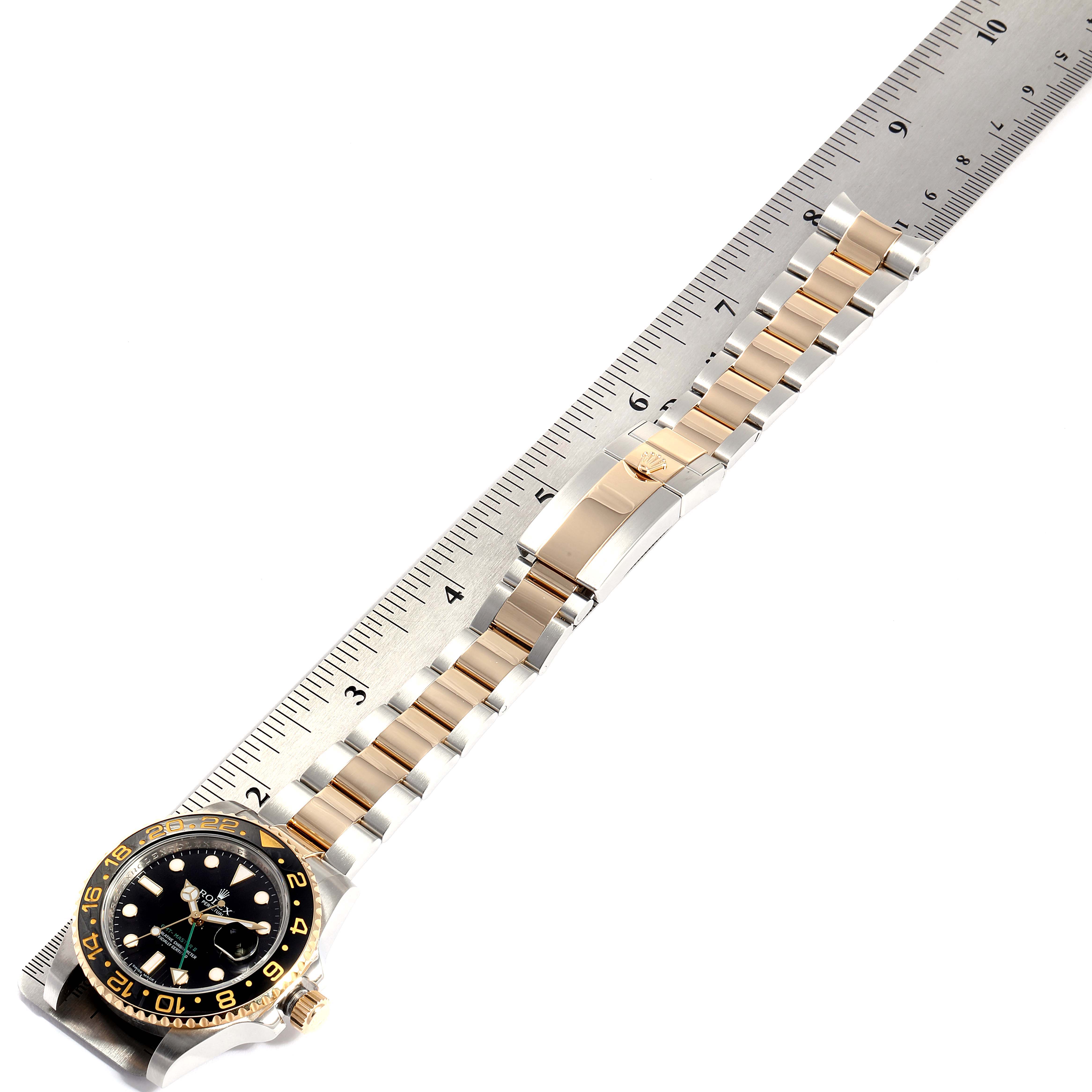 The image shows a Rolex GMT-Master 116713 Men's Steel and Gold (two tone) Black Dial 116713 Men's Steel and Gold (two tone) Black Dial watch placed diagonally, highlighting the bezel, dial, and bracelet alongside a ruler.