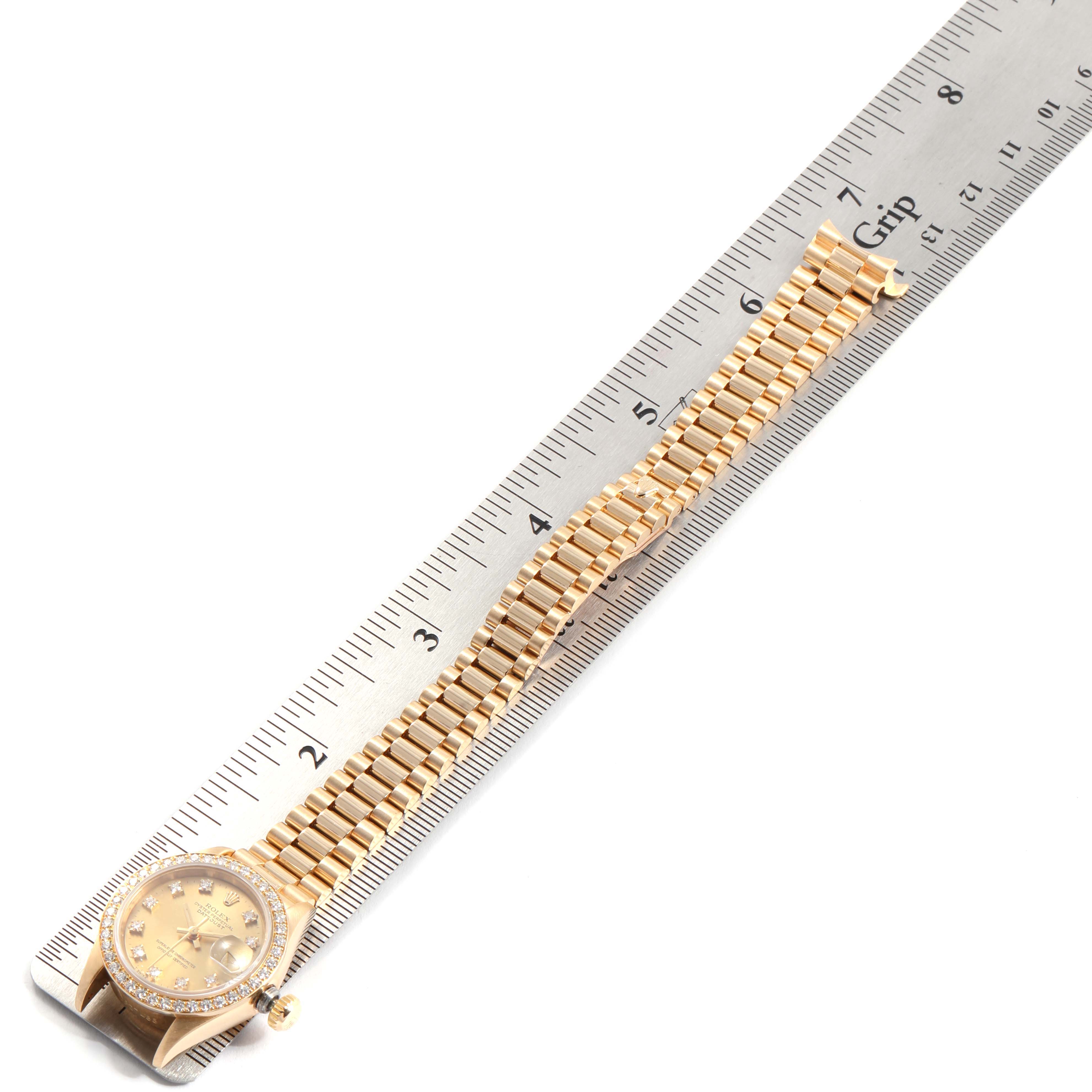 The image shows a Rolex President 69138 Women
s Yellow Gold Champagne Dial 69138 Women
s Yellow Gold Champagne Dial model watch laid flat next to a ruler, displaying the face, band, and clasp.