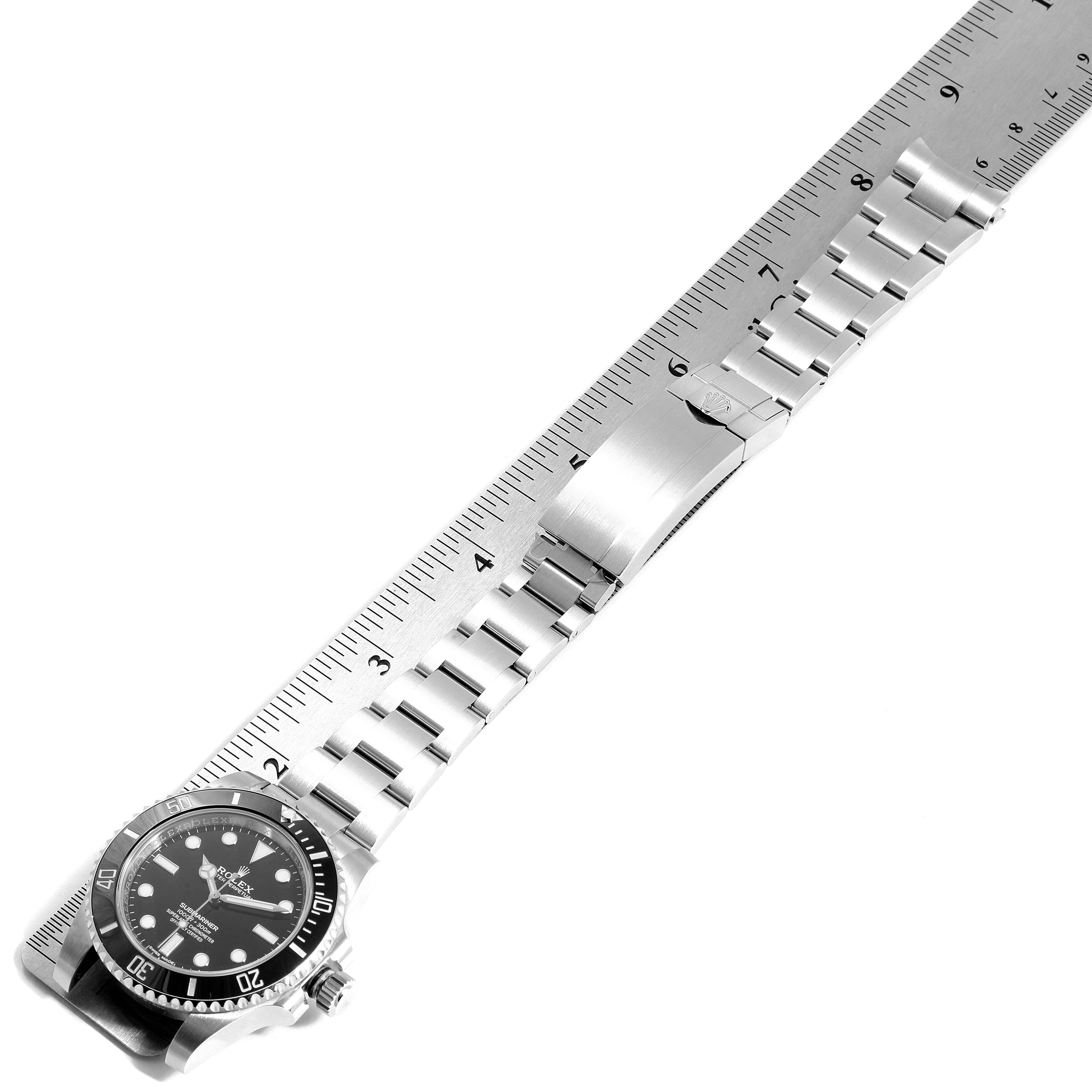 The image shows a Rolex Submariner 114060 Men
s Stainless Steel Black Dial 114060 Men
s Stainless Steel Black Dial watch and its band, aligned with a ruler, viewed from a top-down angle.