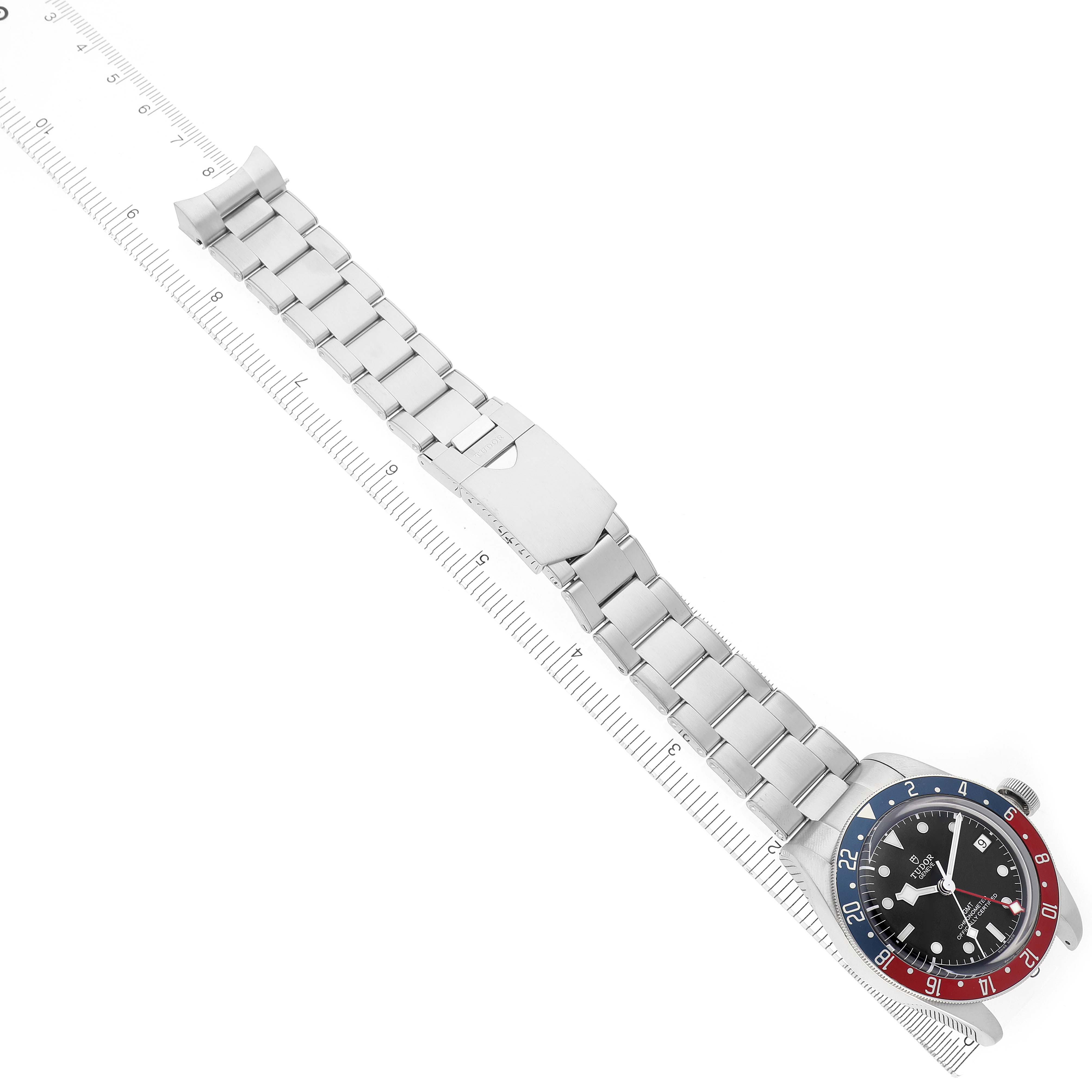 The Tudor Heritage Black Bay 79830RB Men's Stainless Steel Black Dial watch is shown from a top-down angle, displaying the full bracelet and face beside a ruler.