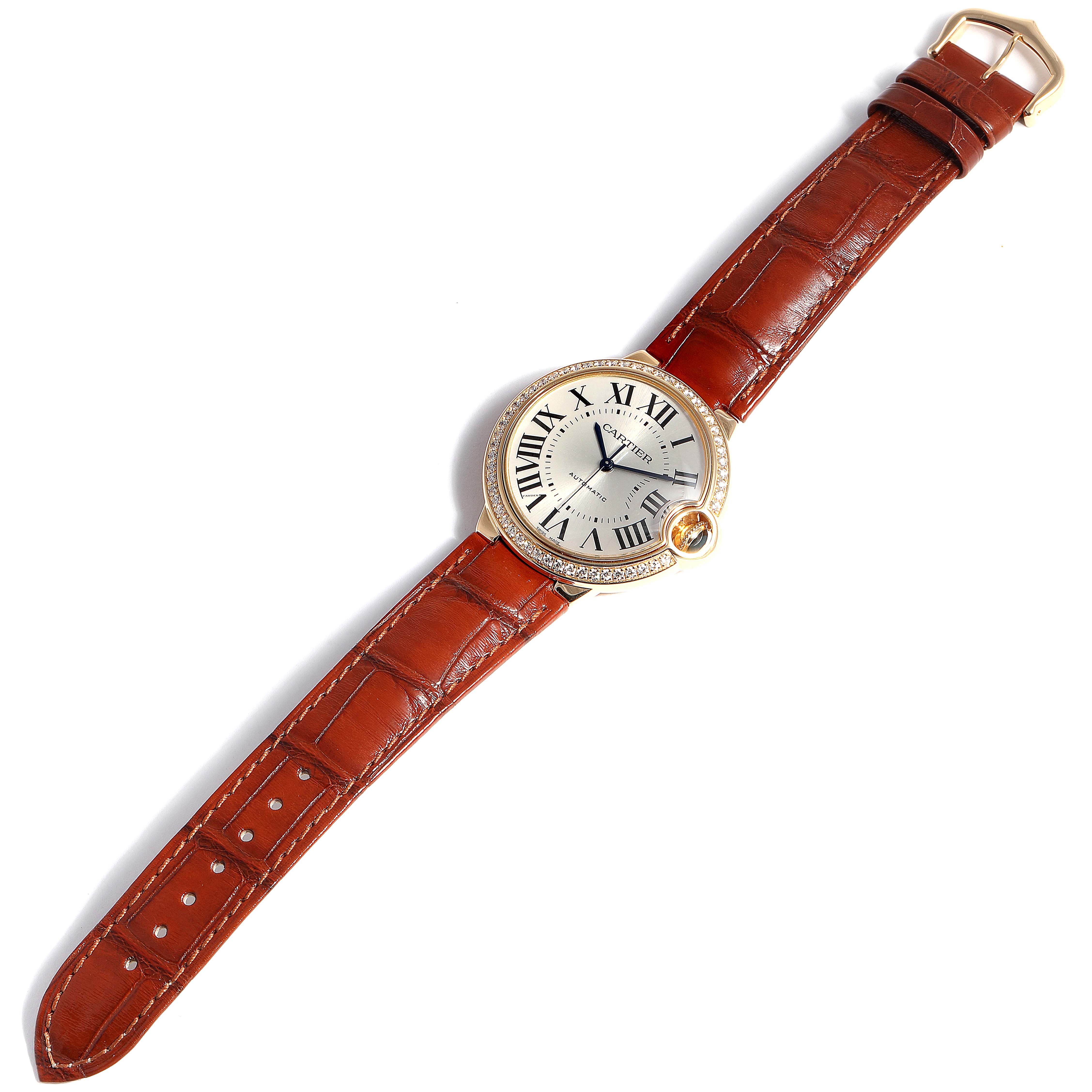 The image shows a Cartier Ballon Bleu WE900451 Women
s Yellow Gold Silver Dial WE900451 Women
s Yellow Gold Silver Dial watch from a top-down angle, highlighting its face, bezel, crown, and brown leather strap.