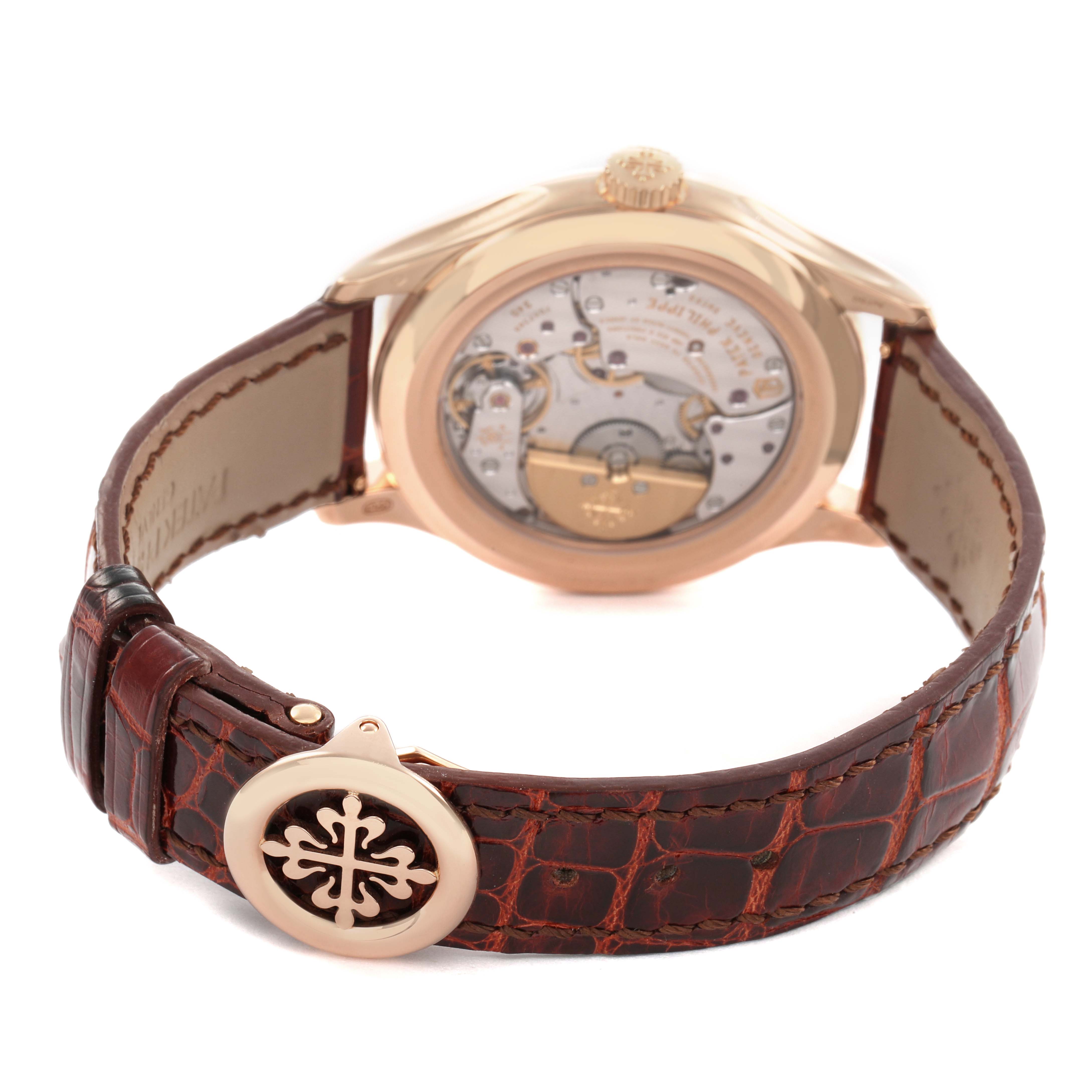 The Patek Philippe Complications 5327R Men's Rose Gold Beige Dial model is shown from the back, highlighting the movement and a brown leather strap with a decorative clasp.
