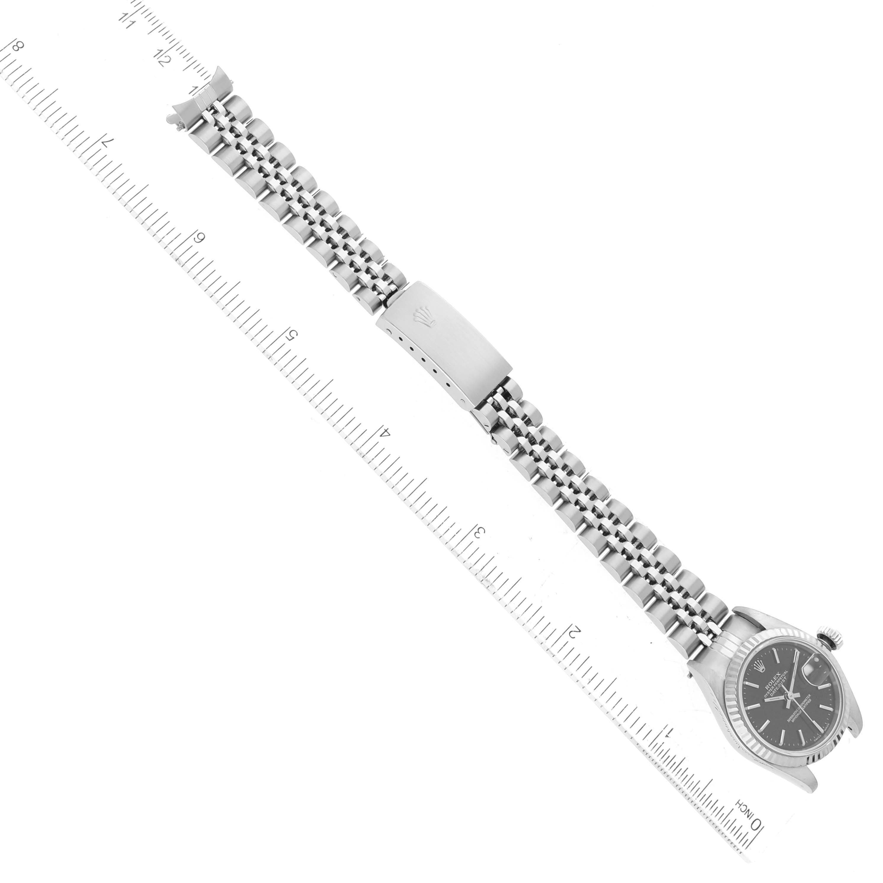 This image shows a Rolex Datejust 79174 Women's Stainless Steel Black Dial 79174 Women's Stainless Steel Black Dial watch along with its bracelet and clasp, laid flat next to a ruler.