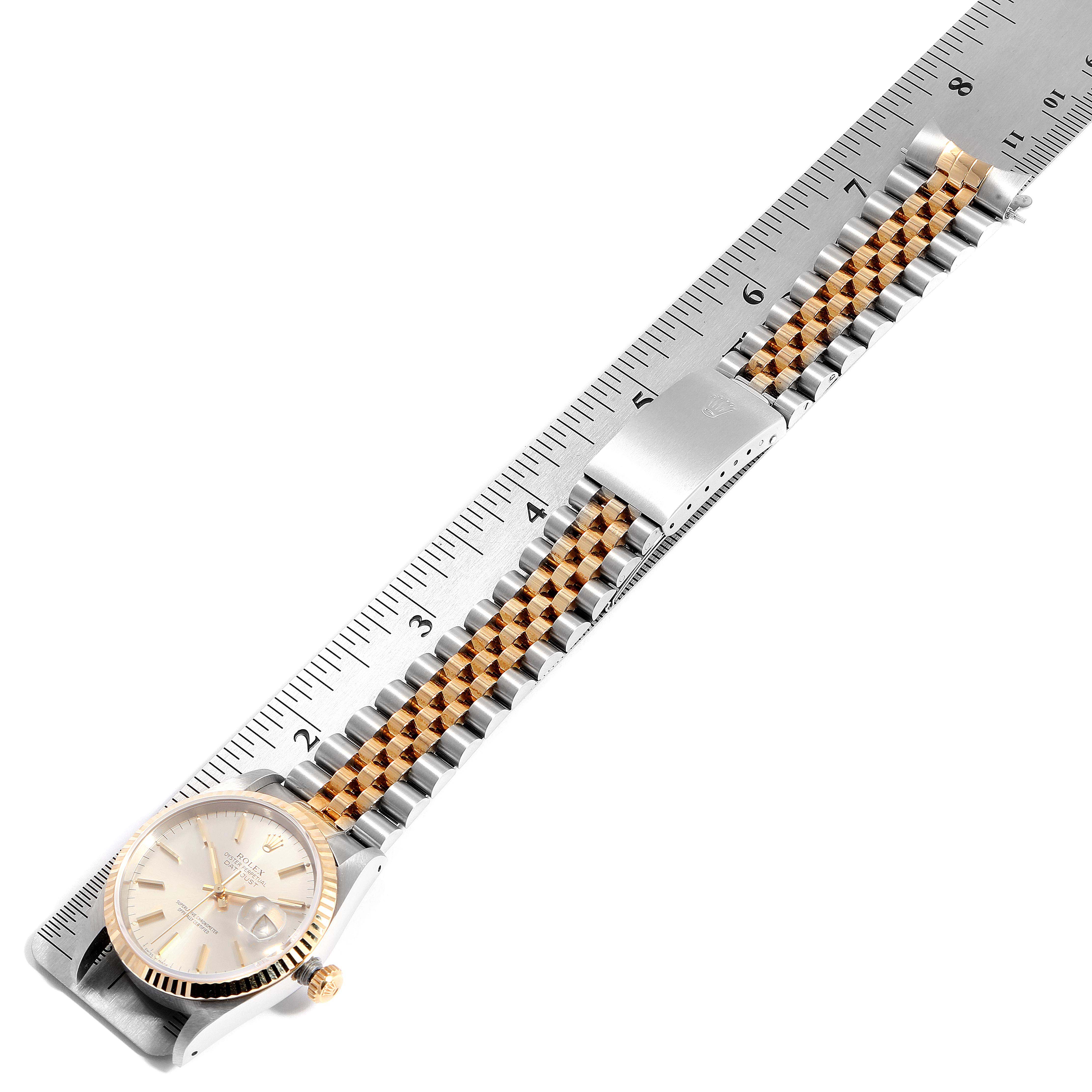 The image shows a Rolex Datejust 16233 Men
s Steel and Gold (two tone) Silver Dial 16233 Men
s Steel and Gold (two tone) Silver Dial watch laid flat on a ruler, displaying the face, bezel, crown, and the full bracelet.