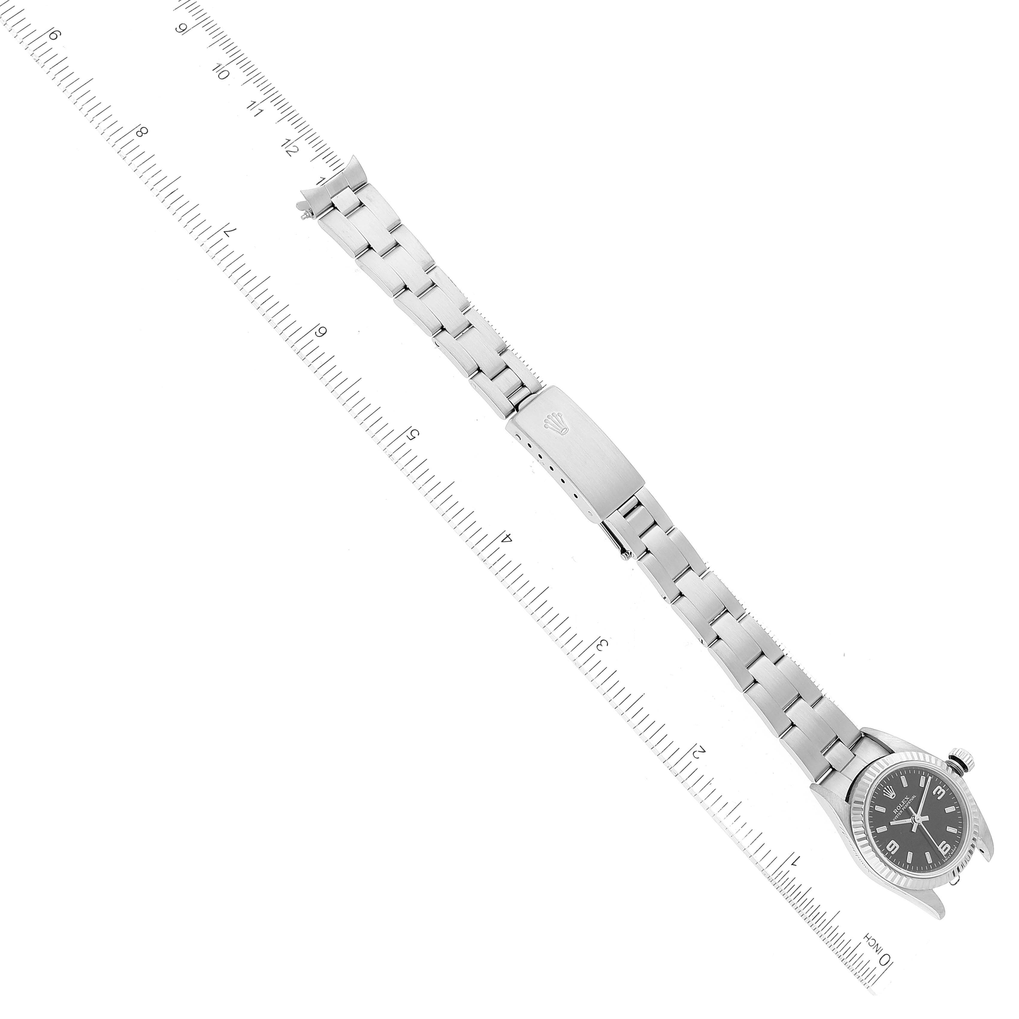 The image shows the Rolex Oyster Perpetual 76094 Women's Stainless Steel Black Dial 76094 Women's Stainless Steel Black Dial watch lying flat with its full band and clasp visible, alongside a measuring ruler.