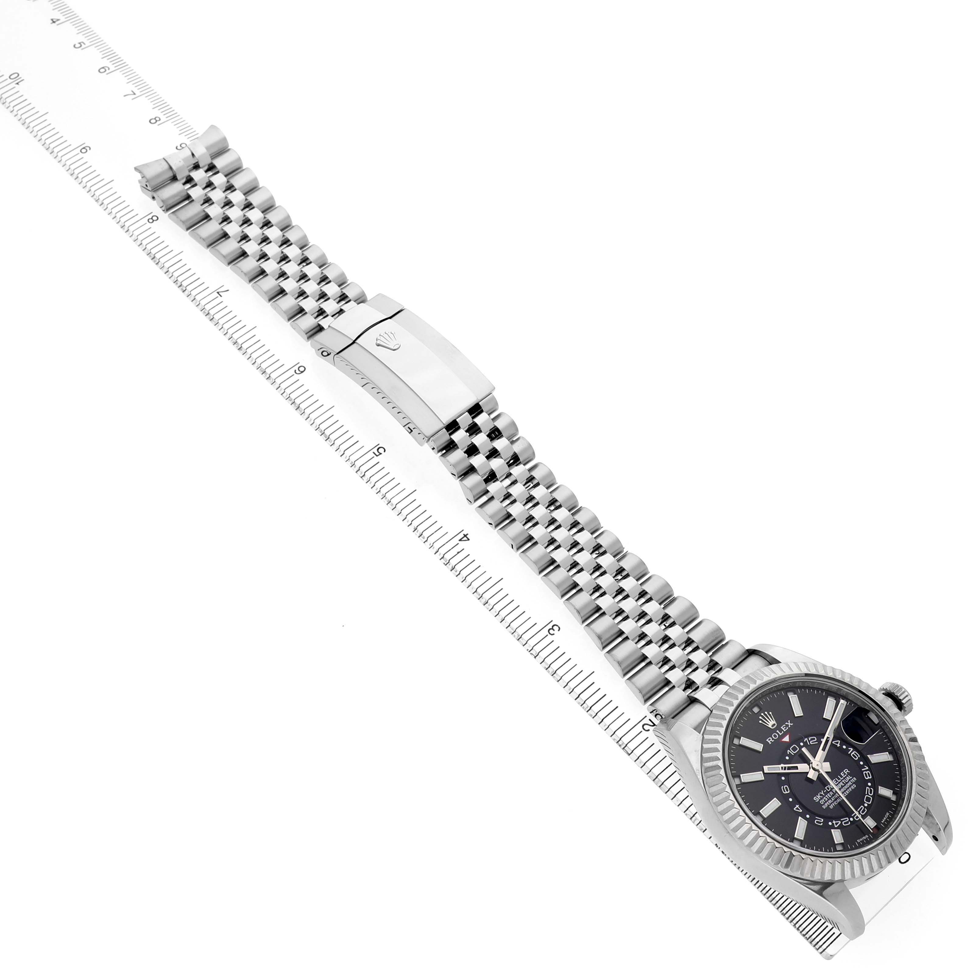 The Rolex Sky-Dweller 326934 Men's Stainless Steel Black Dial watch is shown with a top view, displaying its face, bezel, bracelet, and clasp next to a ruler.